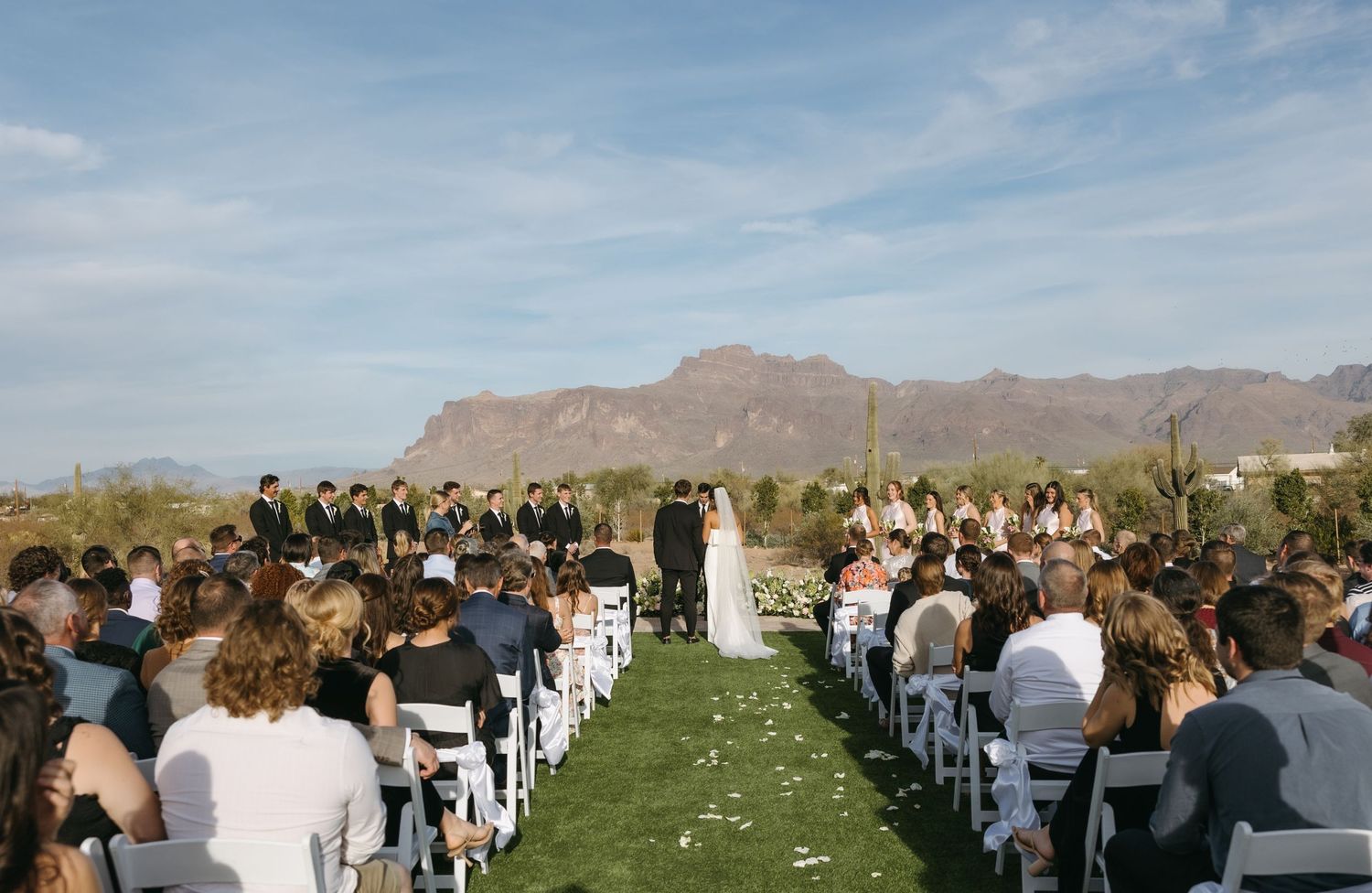 An outdoor desert wedding ceremony with mountain backdrop and rows of seated guests.