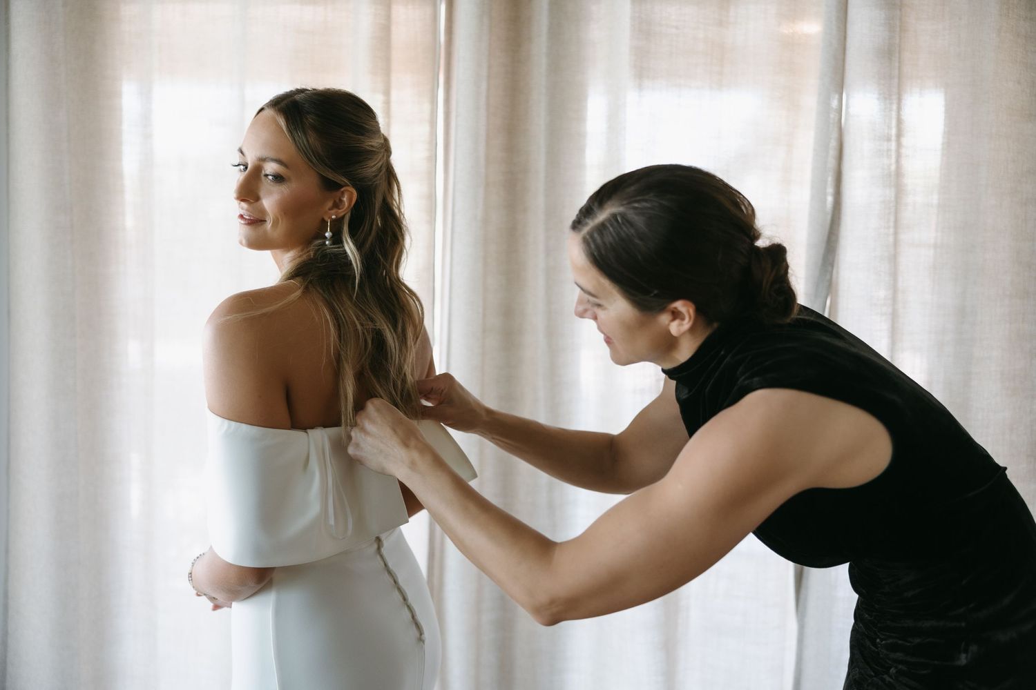 Wedding dress fitting moment captured near a sunlit window.