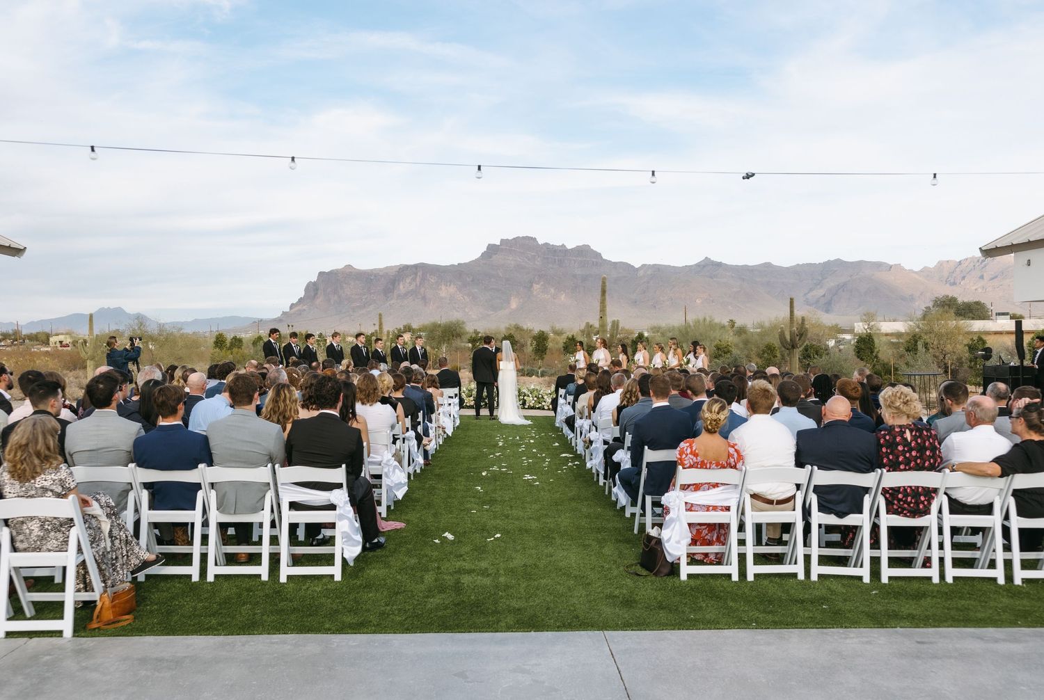 Desert wedding ceremony with mountain views and rows of white chairs filled with guests.