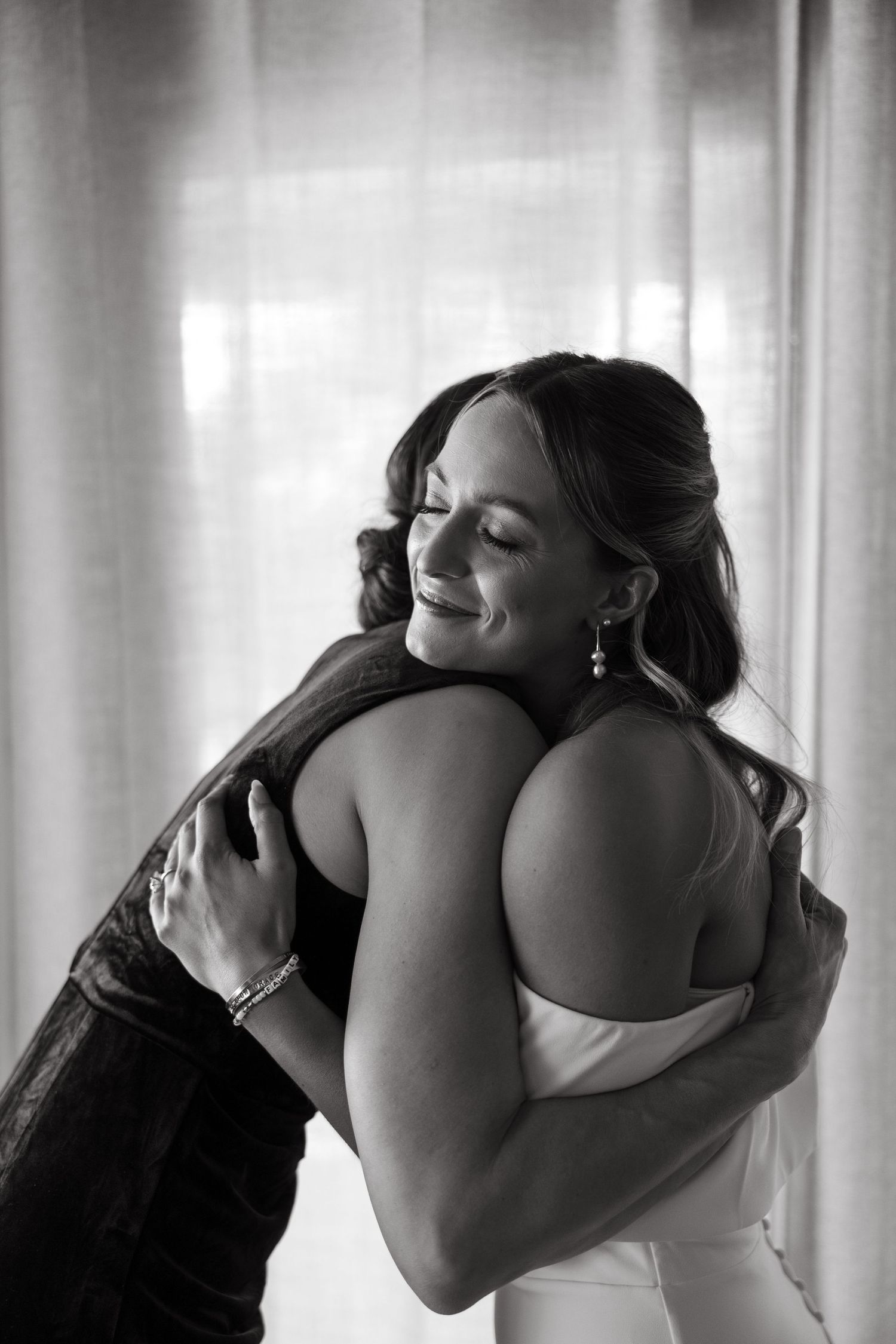 Emotional black and white wedding day embrace captured by window light.
