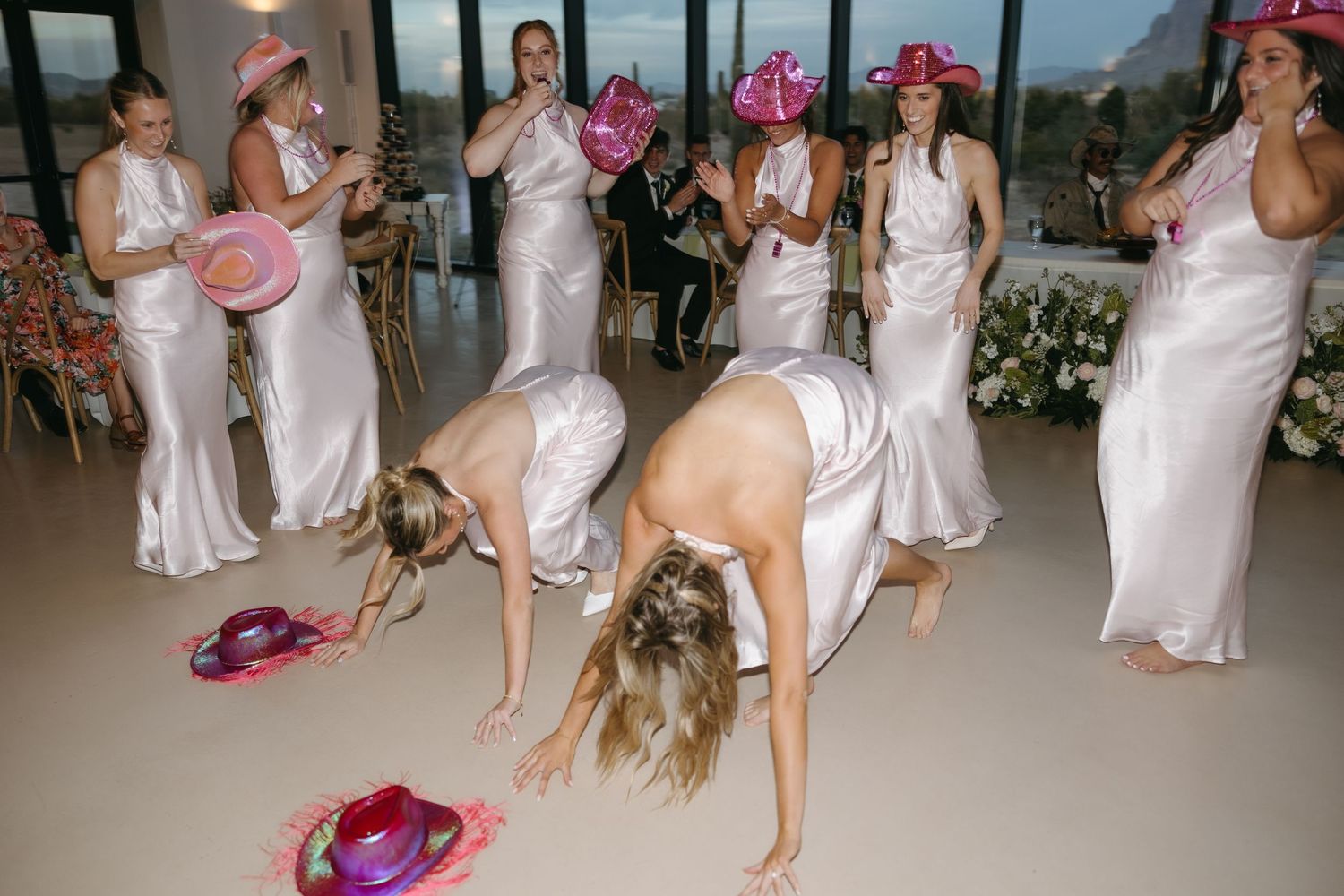 Bridesmaids in white dresses playing a fun party game at a wedding reception.