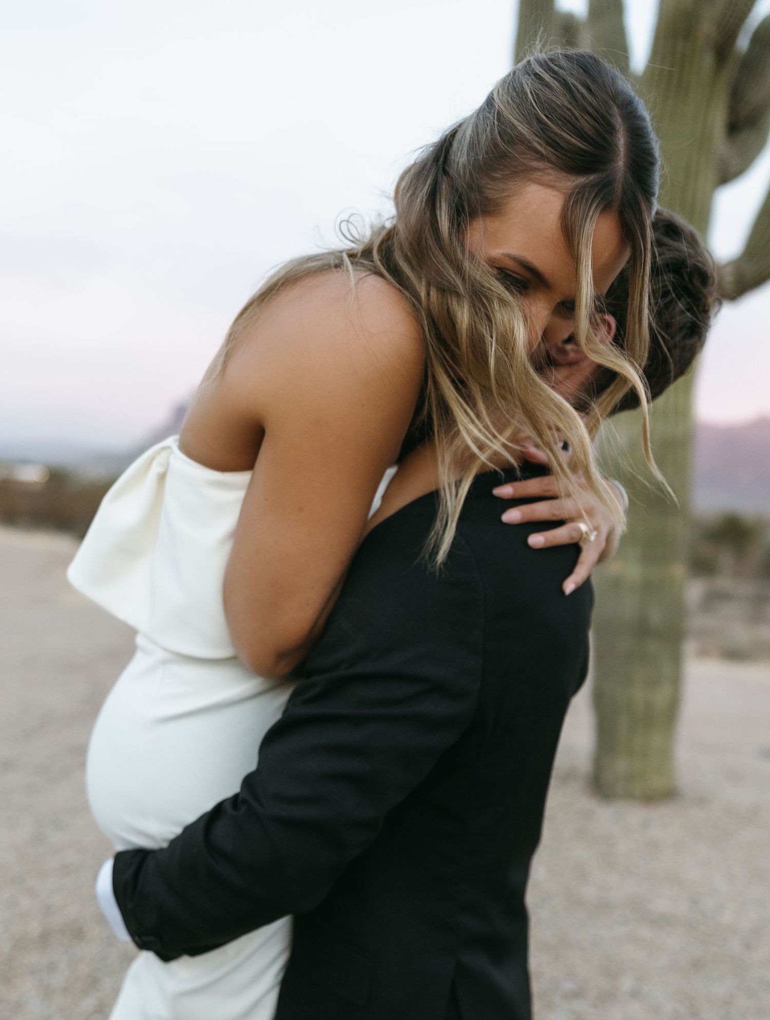 Romantic embrace between couple against desert backdrop with saguaro cactus.