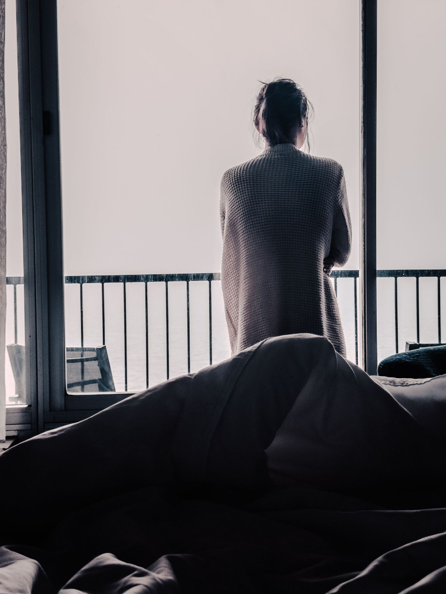 A silhouetted figure stands at a balcony railing looking out into the distance.
