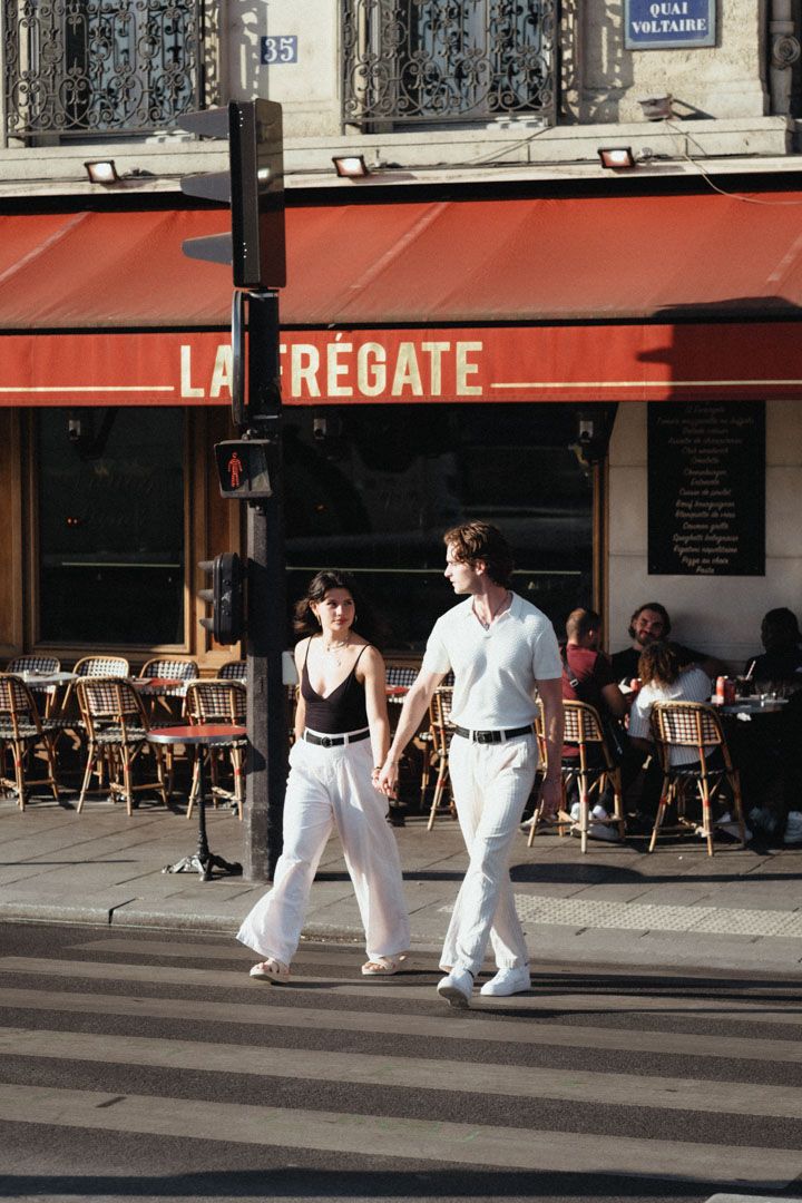 People walking past a classic Parisian cafe with red awning and outdoor seating.