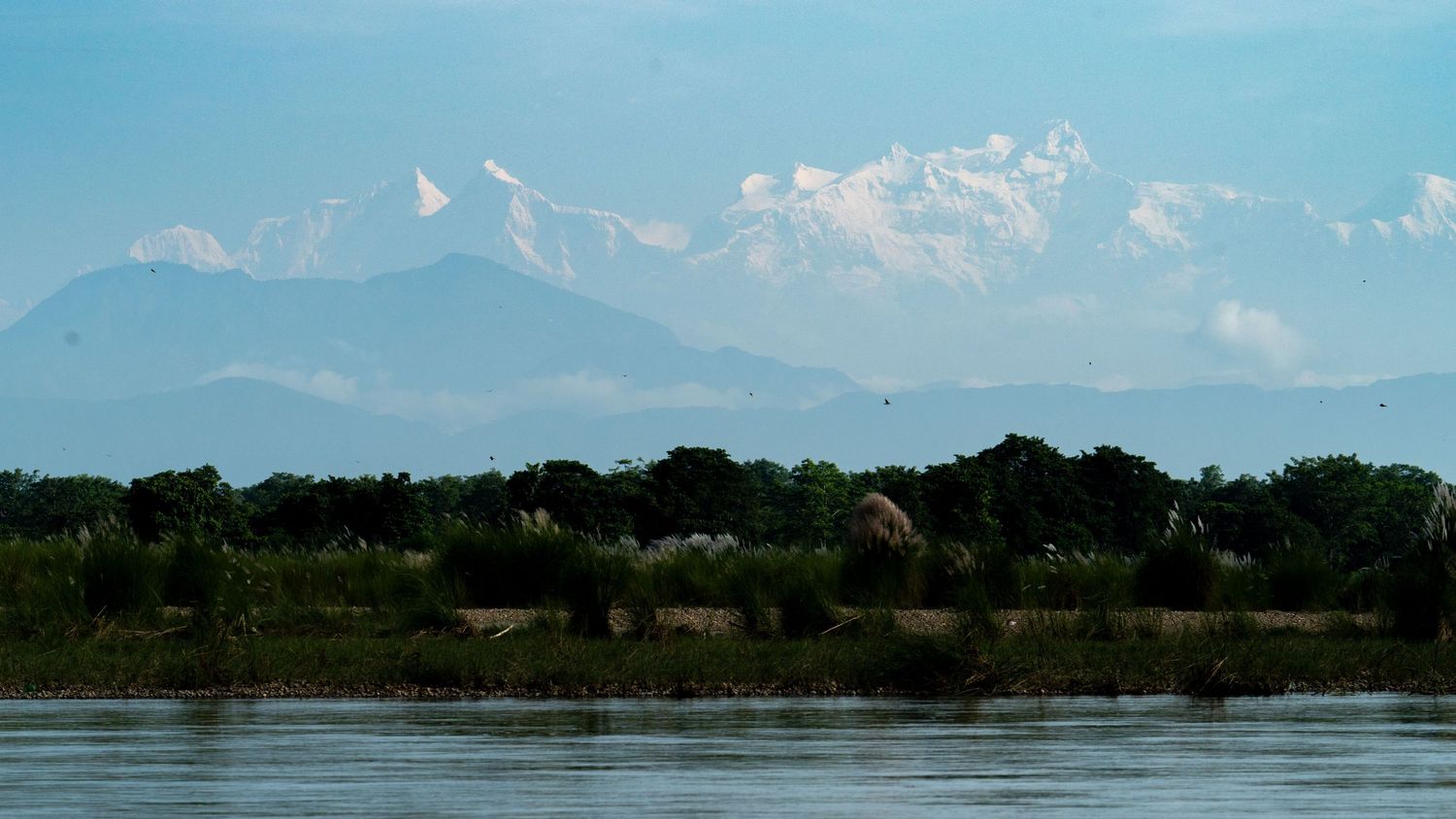 Panoramic mountain landscape with lake and trees under bright blue sky.