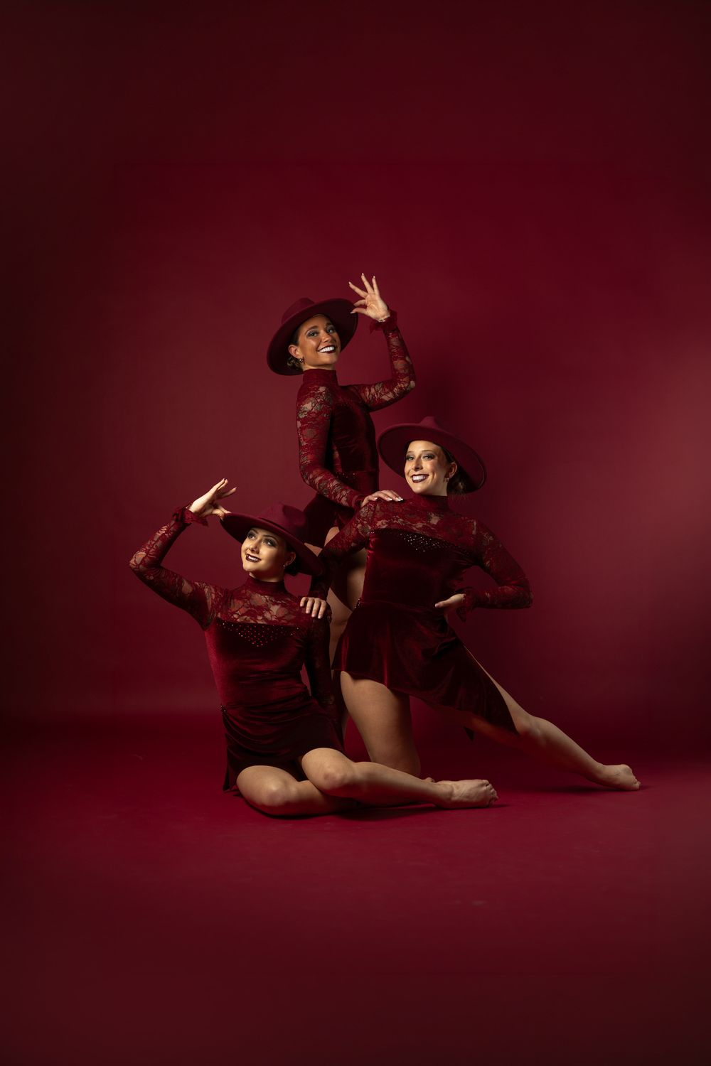 Three dancers in matching red velvet costumes and hats strike elegant poses against a deep red background.
