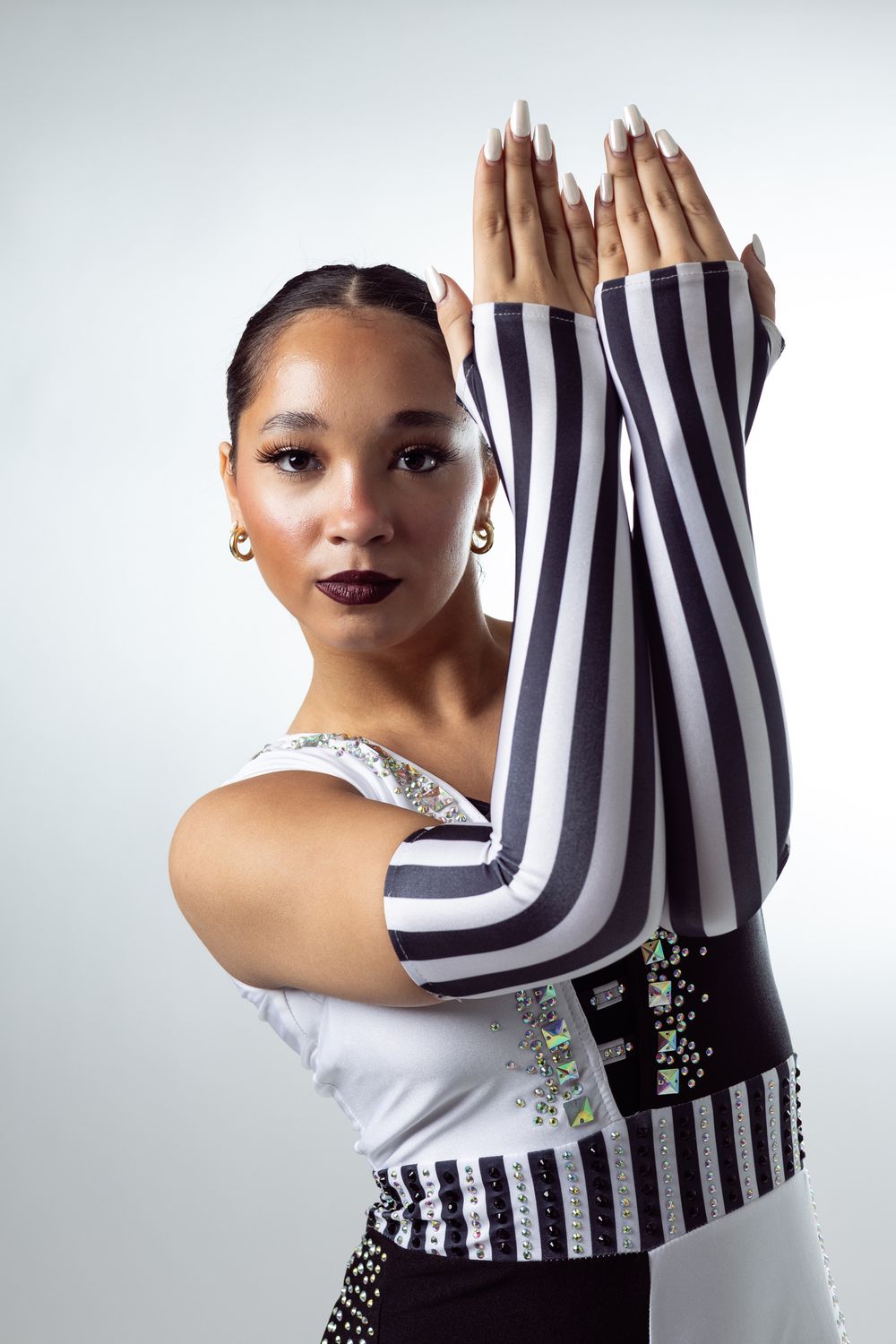 Young woman in black and white striped arm sleeves poses gracefully with hands raised, wearing elegant gold earrings.