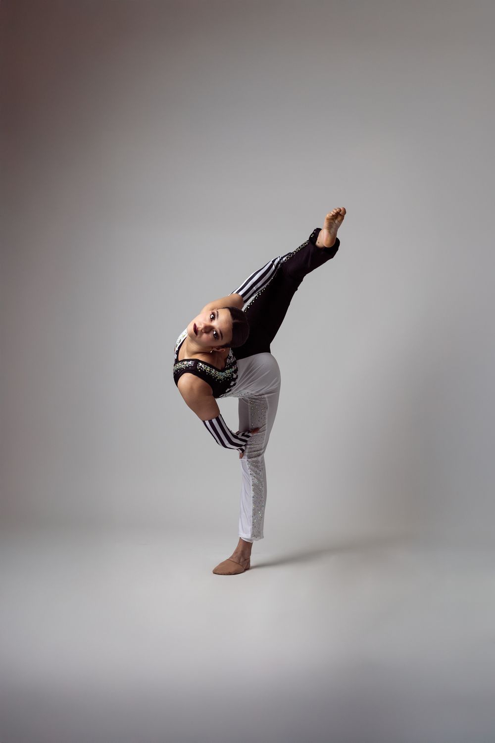 Flexible dancer in white pants performs a standing split pose in a studio setting.