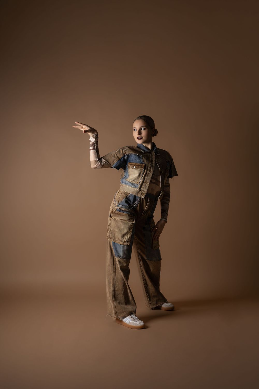 Model in distressed denim cargo outfit pointing sideways against brown background.