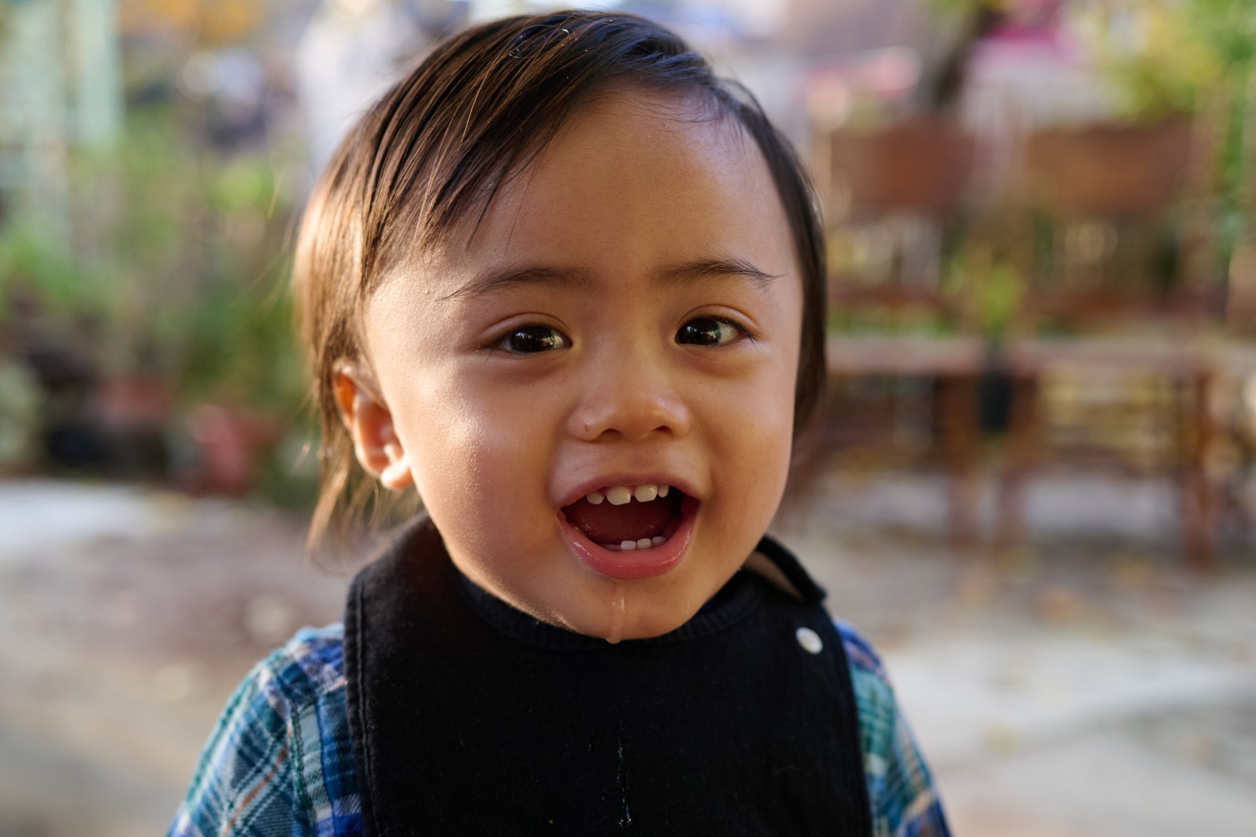 A joyful child wearing a plaid shirt smiles brightly outdoors on a sunny day in at Weston Ranch California.