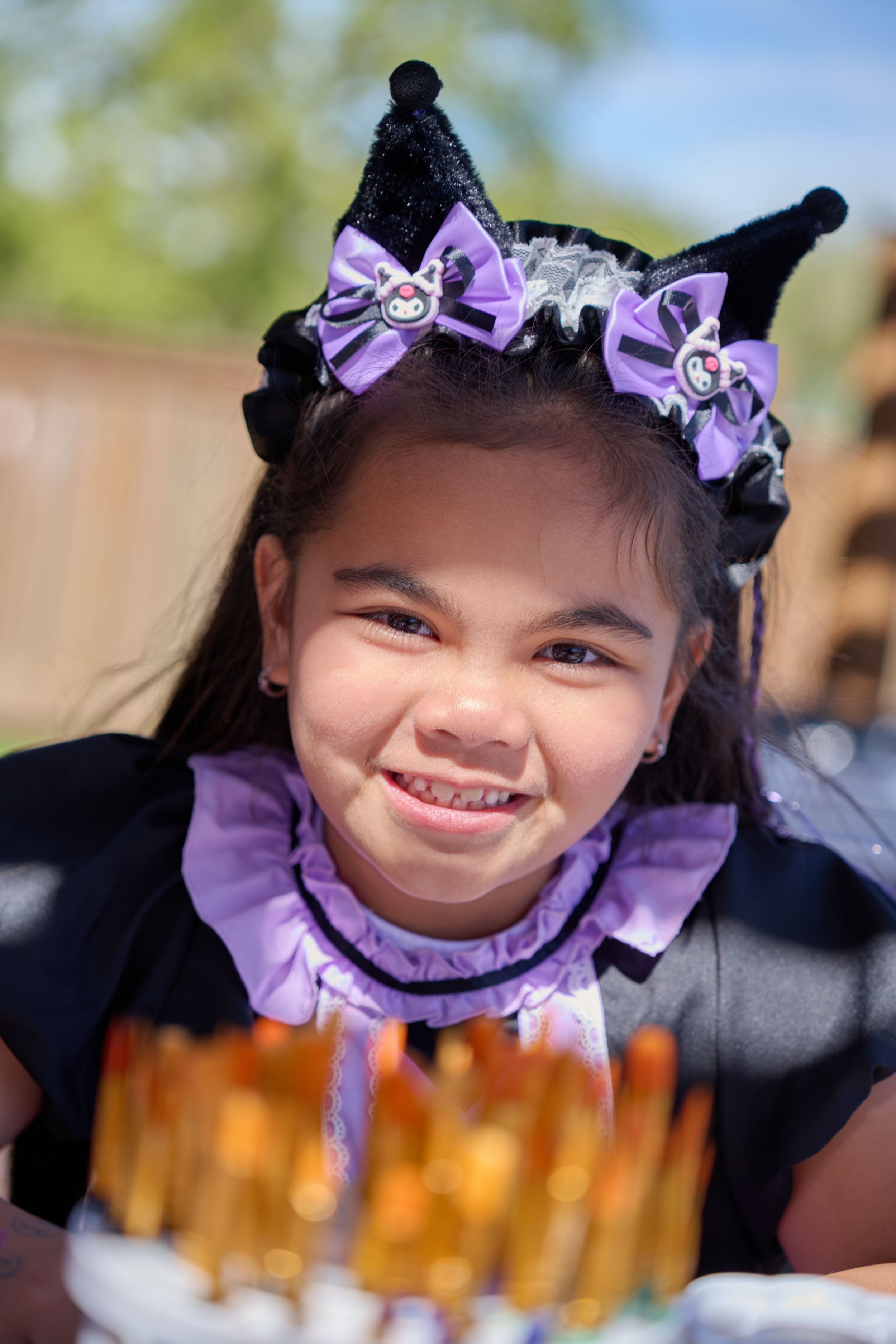 A child wearing purple bows and black cat ears enjoys a festive birthday celebration with a cake in front of them.