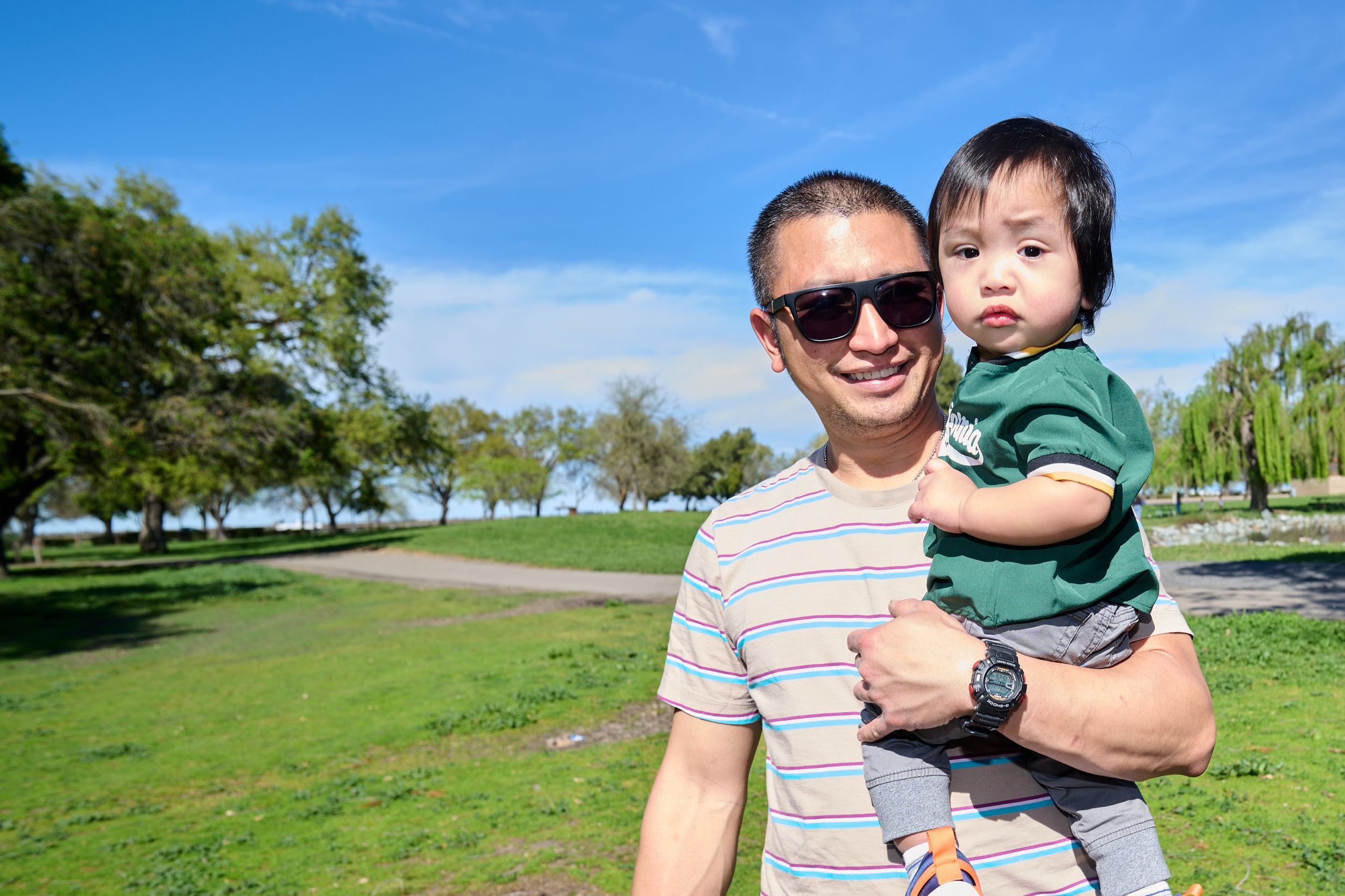 People enjoying a sunny day at a park with green grass and trees in the background.
