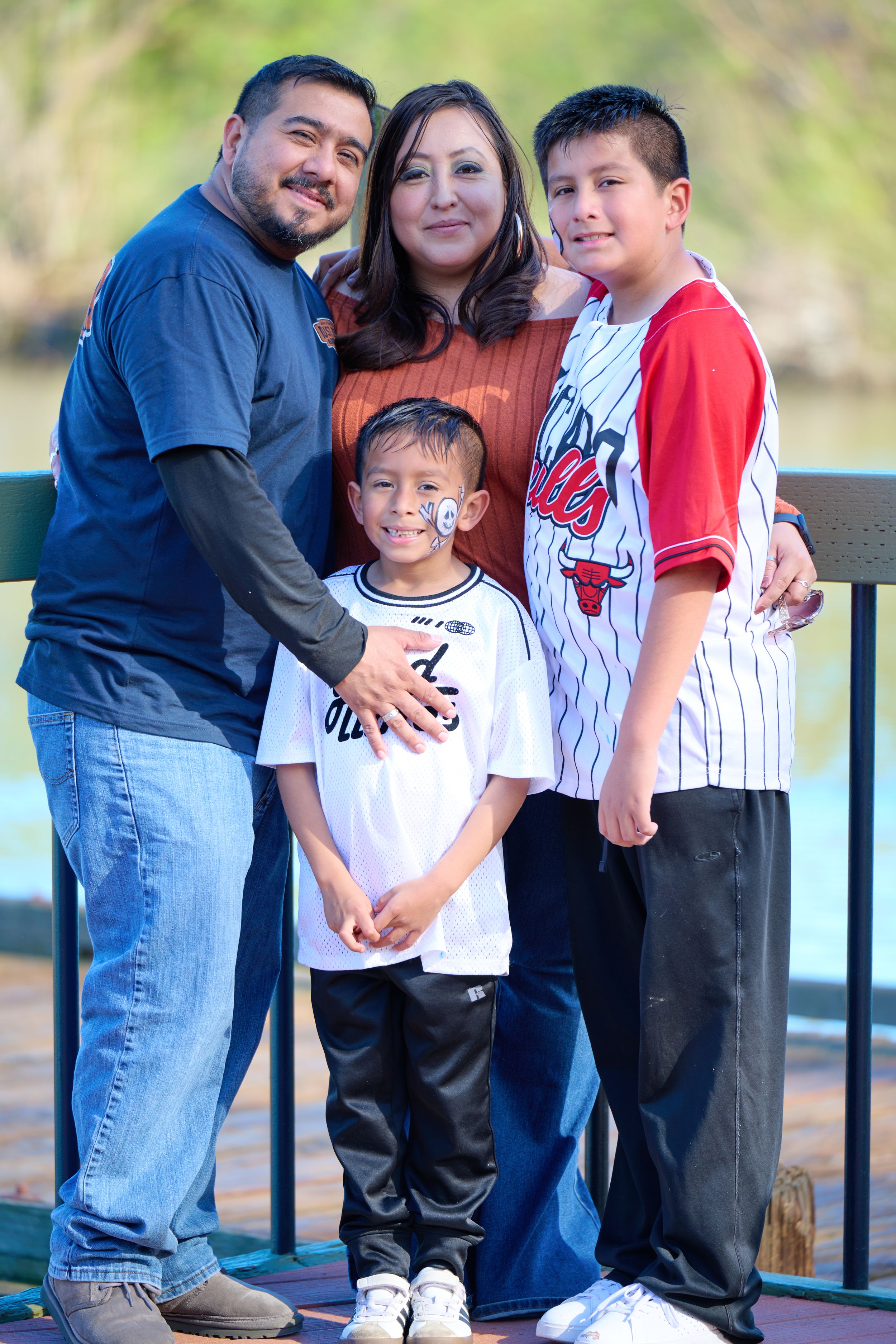 A family of four poses together outdoors on a sunny day wearing baseball-themed attire at a park.