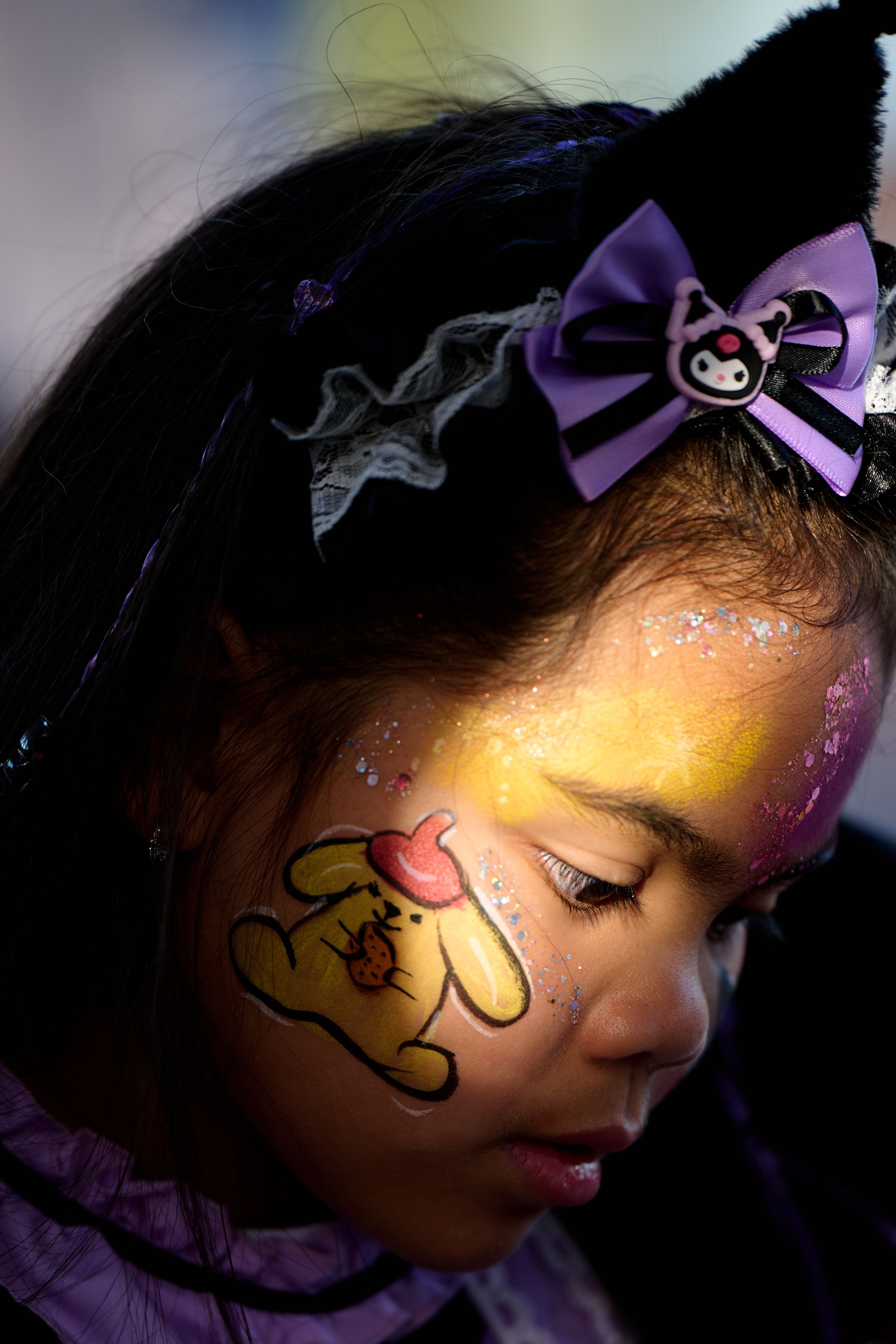 Child with purple hair bow and face paint of a puppy design illuminated by warm lighting against dark background.