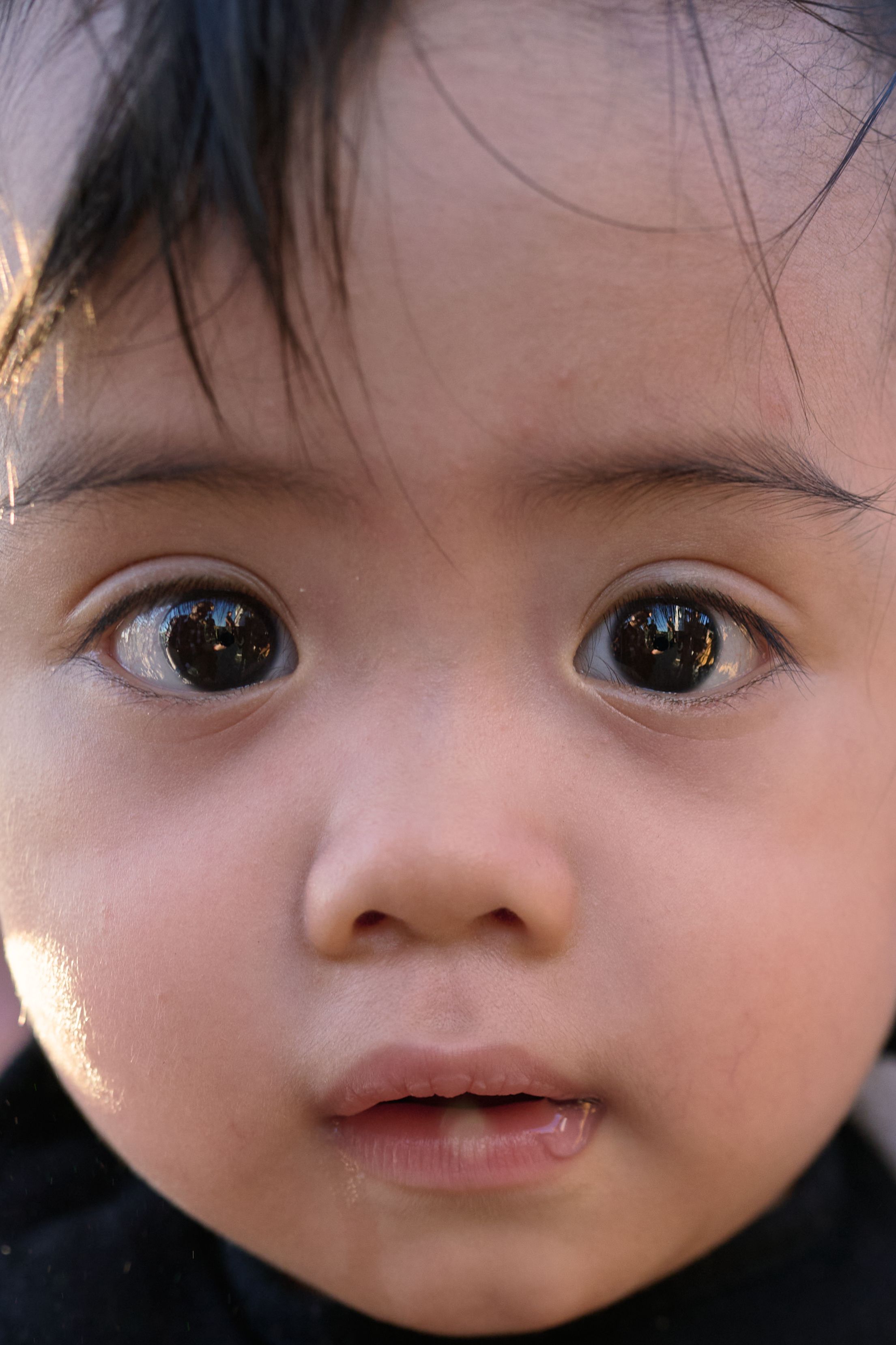 Close-up photo of a young child with large brown eyes, dark hair, and soft lighting on their face.