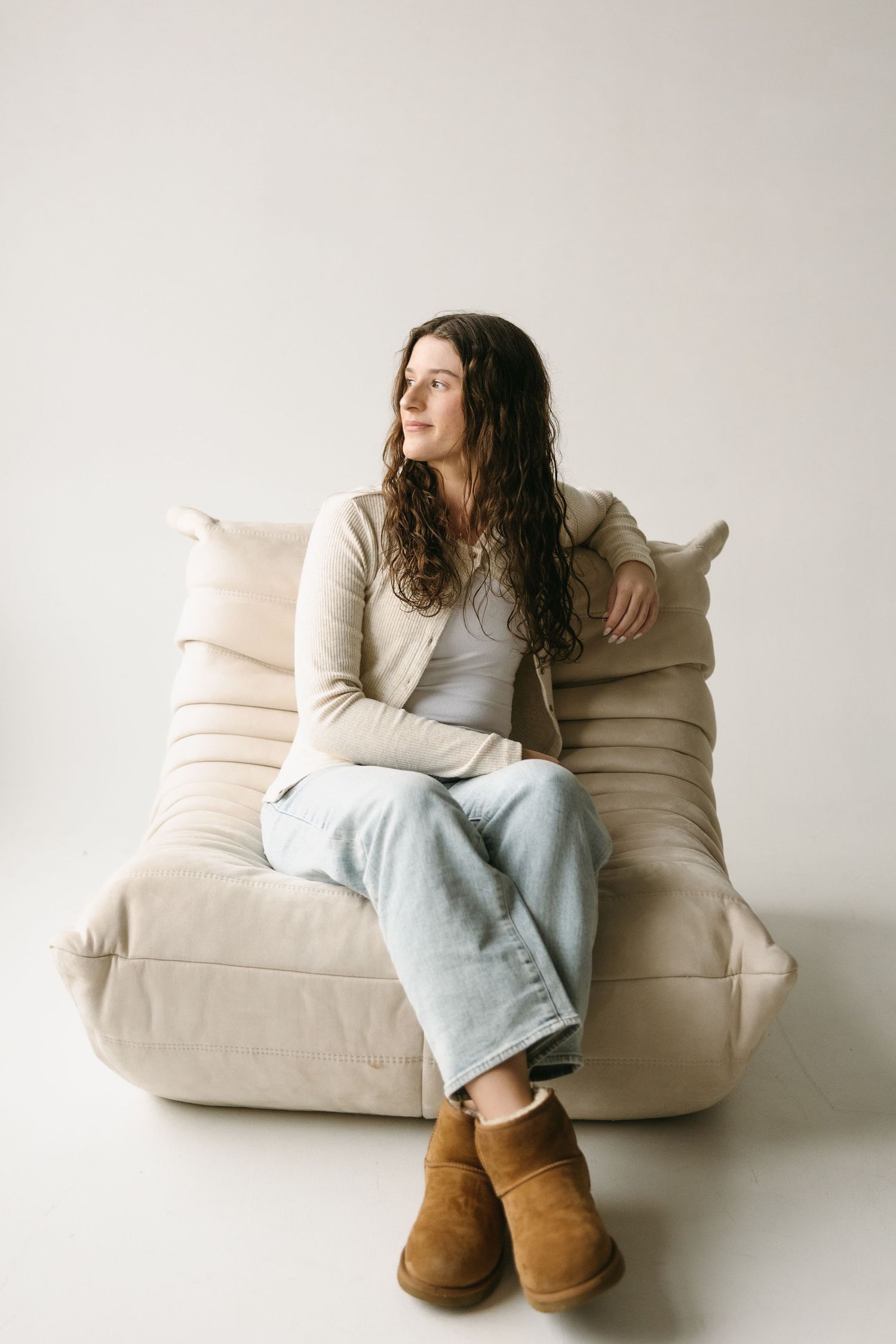 Cozy lifestyle portrait on beige floor cushion wearing cream cardigan and light denim with brown boots.