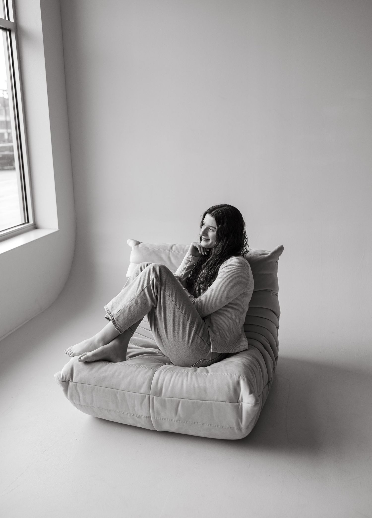 Minimalist black and white portrait on floor cushion by window in casual loungewear.