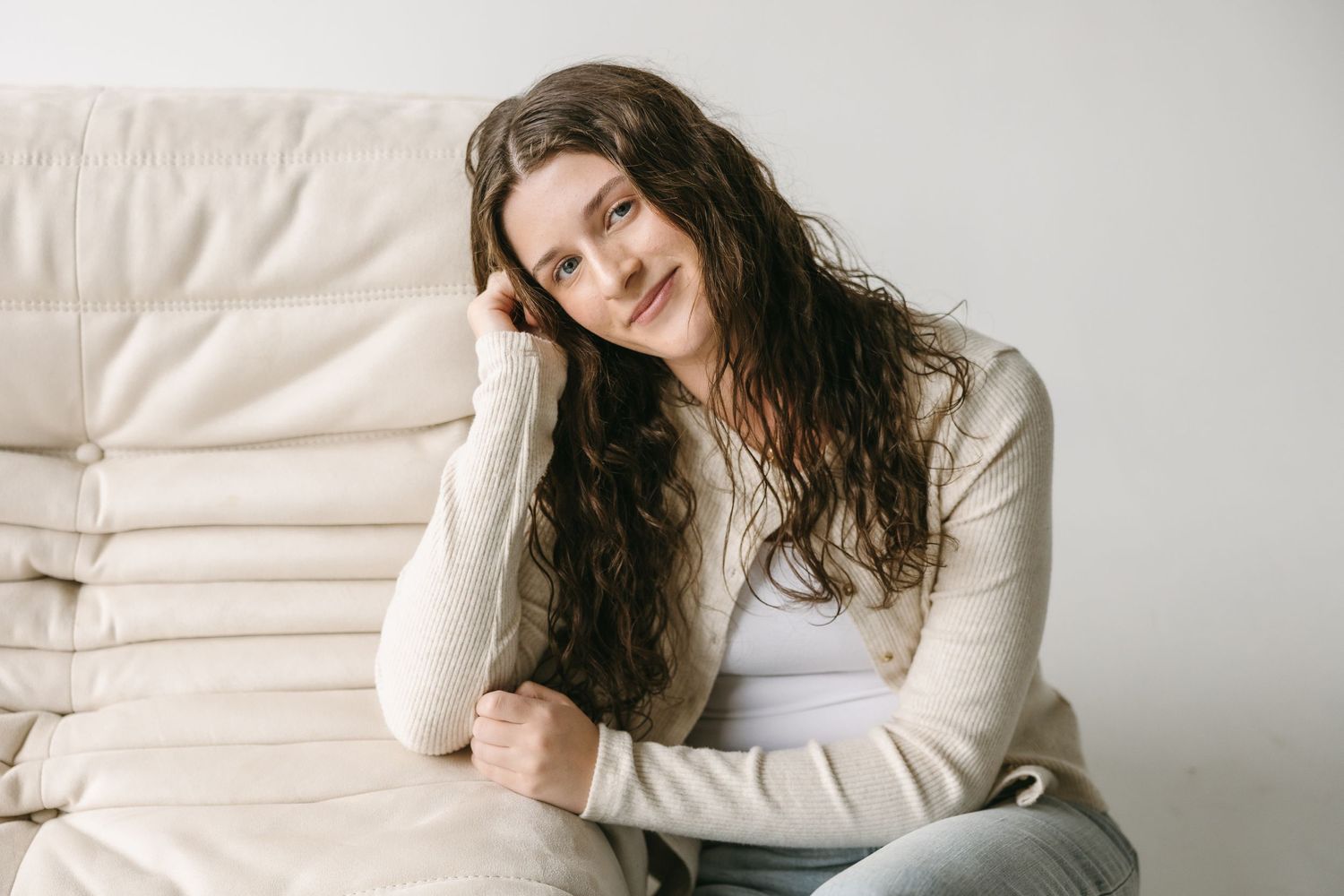 Person relaxing on white couch wearing cream sweater and casual attire in cozy indoor setting.