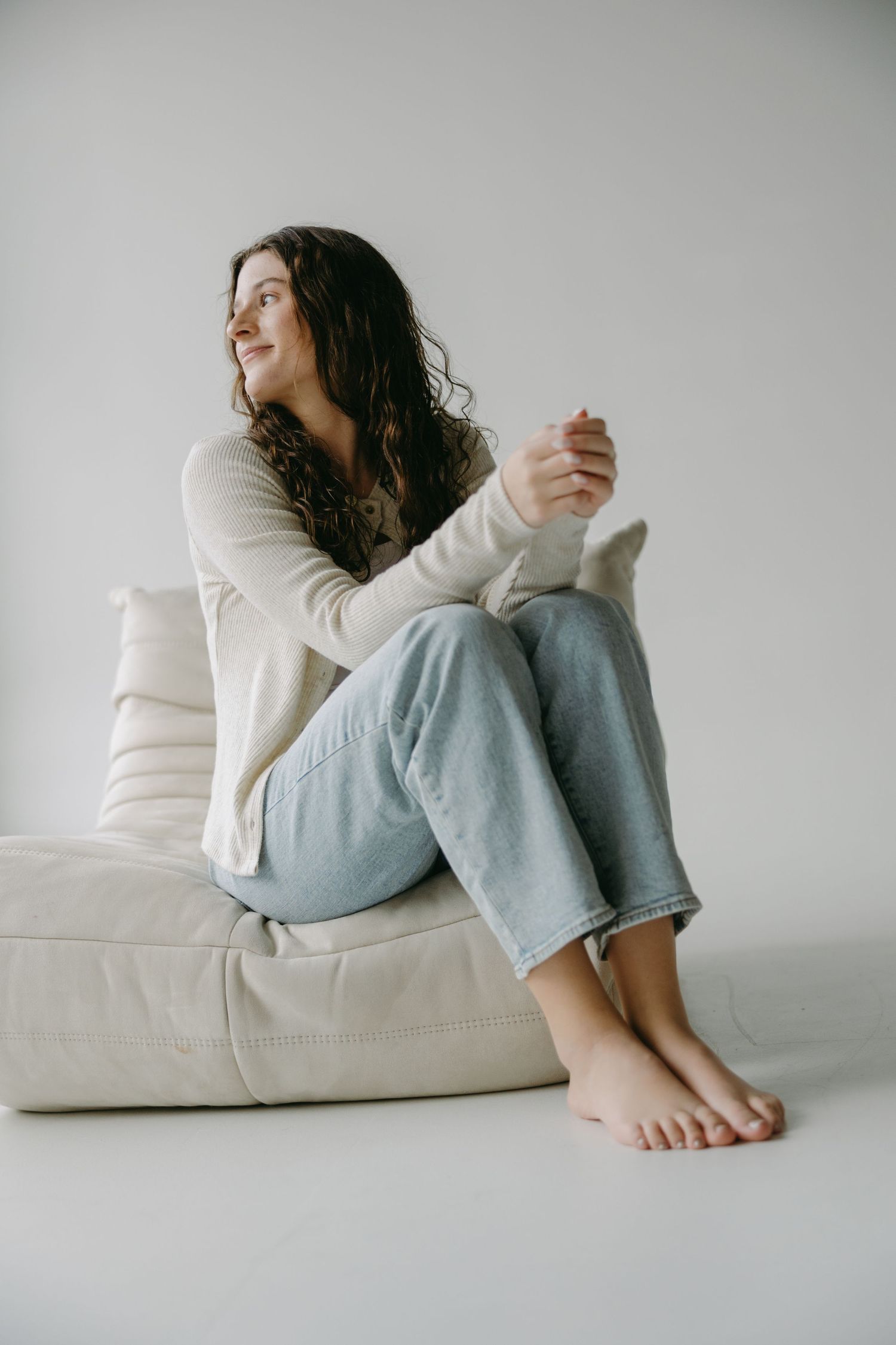 Candid portrait on beige cushion wearing cream sweater and light denim with natural styling.