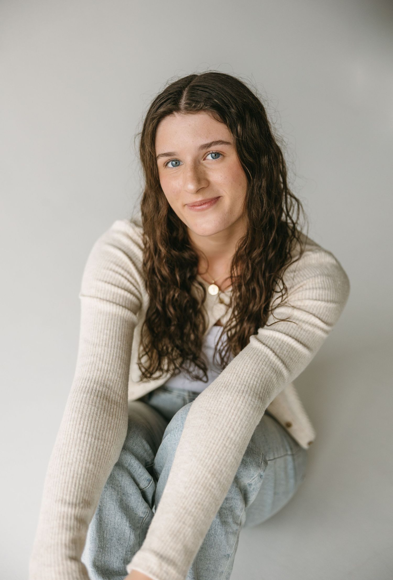 Casual portrait against white wall wearing cream knit cardigan with relaxed styling.