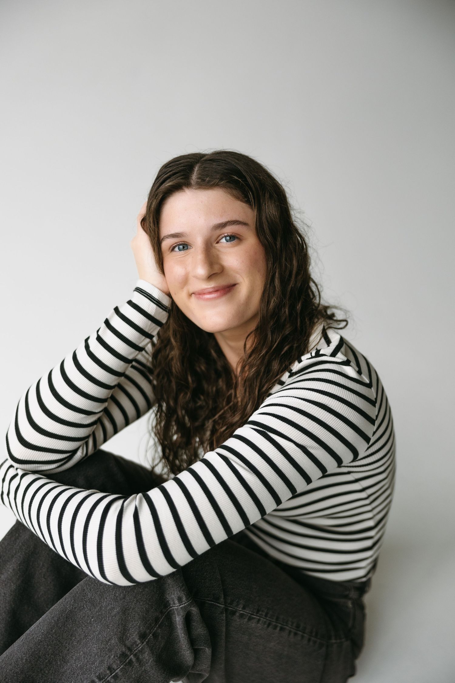 Studio portrait of person in black and white striped top smiling against white wall.