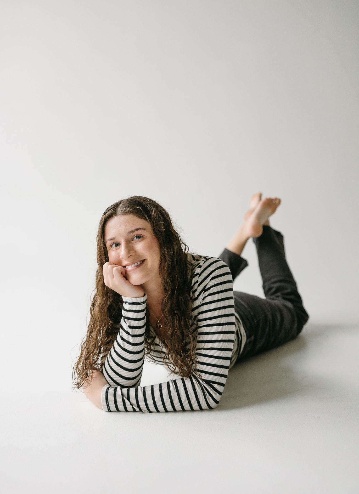 Relaxed portrait of person lying on white floor wearing striped top and dark pants.