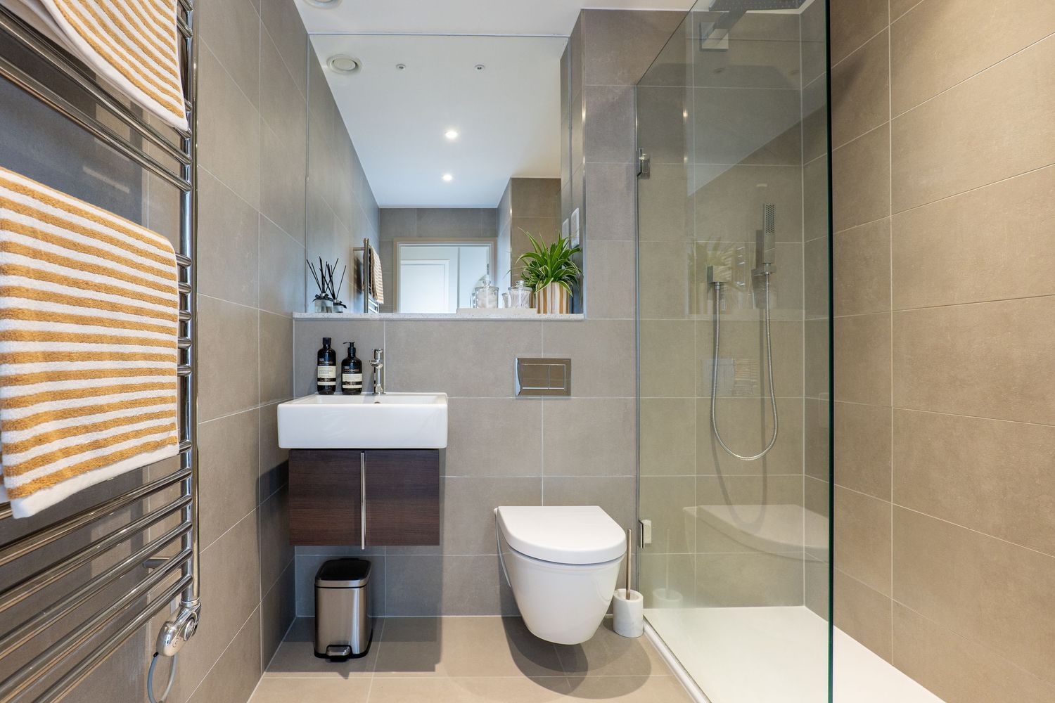 Modern bathroom interior with glass shower enclosure, neutral beige tiles, and wooden window blinds.