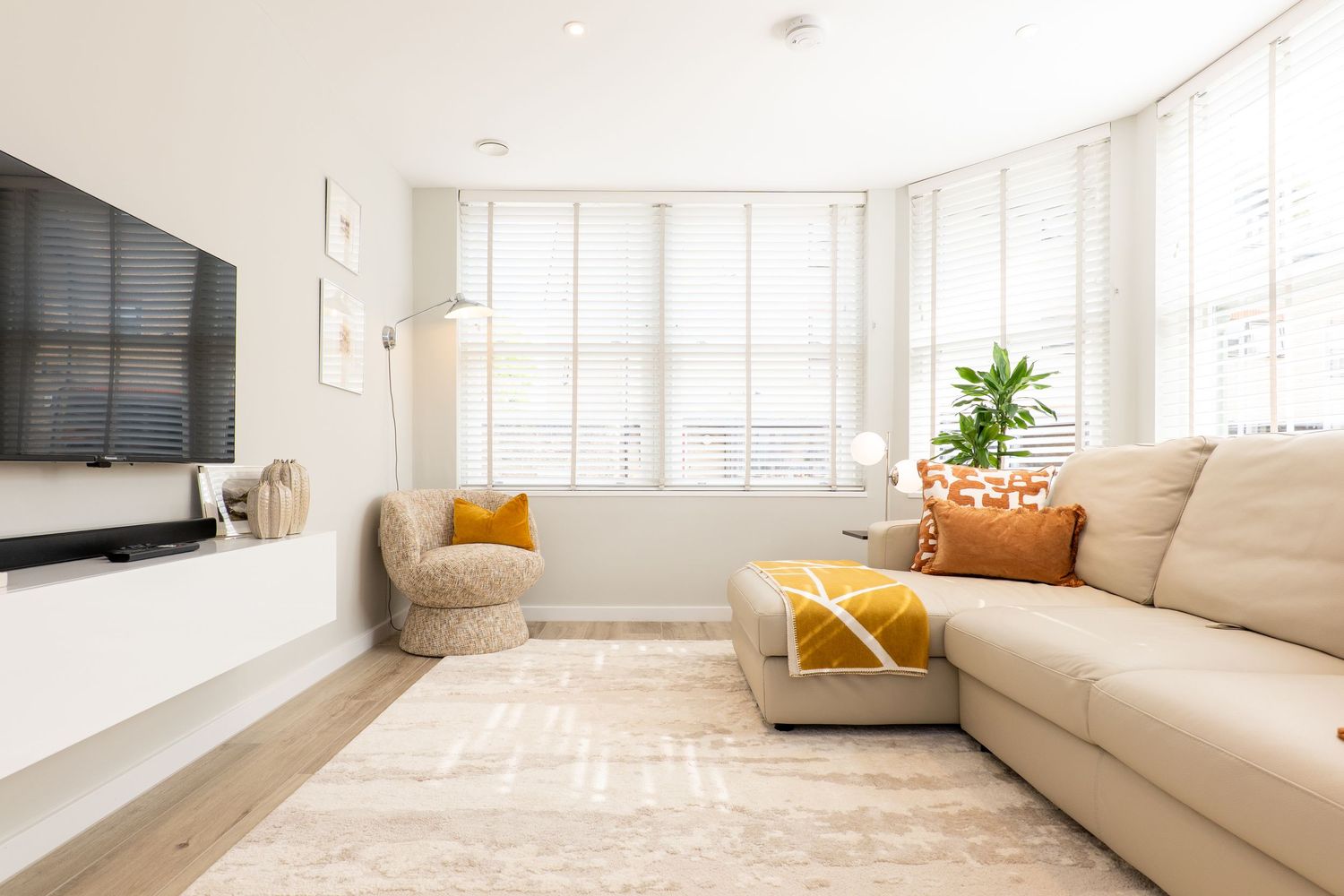 Modern minimalist living room with open floor plan, beige sofa, wood floors, and bright natural lighting throughout.