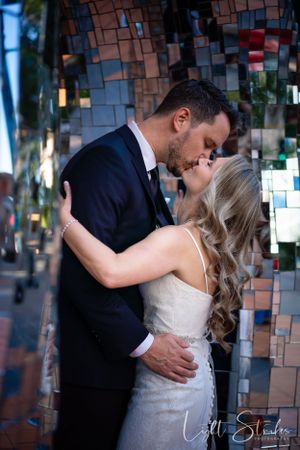 A couple shares an intimate kiss against a sparkling mosaic wall backdrop at a wedding celebration captured by wedding photographer near me.
