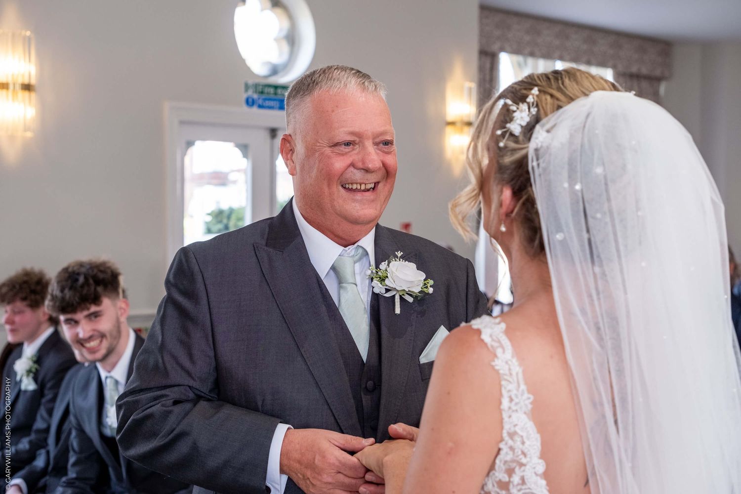 A touching moment at a wedding ceremony shows two people sharing a joyful exchange under indoor lighting.