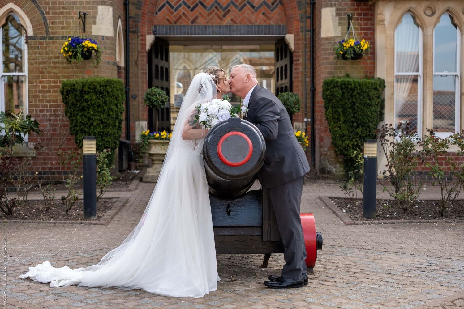 A couple shares a romantic moment on a decorative vintage bench outside a brick church with gothic architectural details.