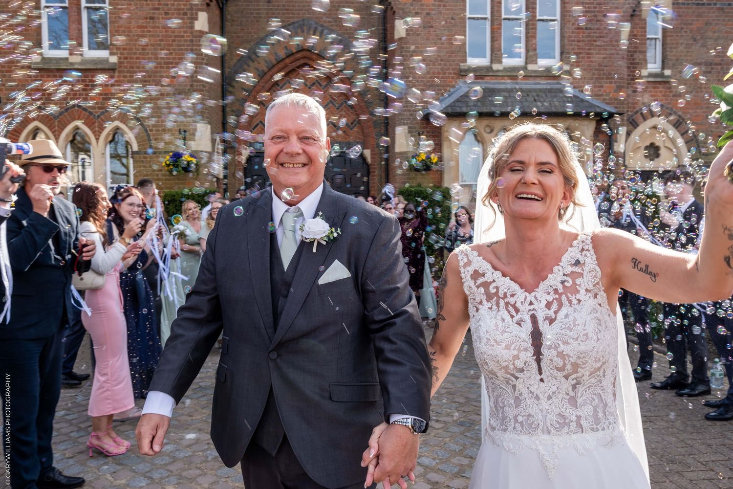 A happy couple exits their wedding ceremony as guests throw confetti outside a brick church building.