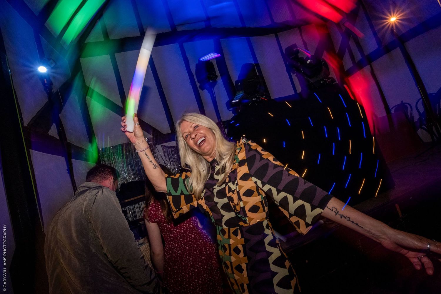 Person in leopard print celebrates at a nightclub with a glowing light stick under colorful lighting effects.