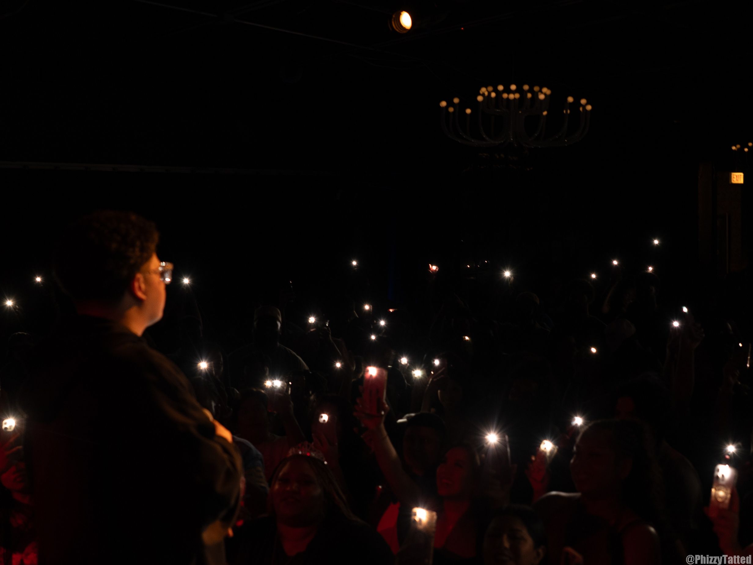 Nighttime crowd scene with twinkling lights and glowing phones in the darkness.