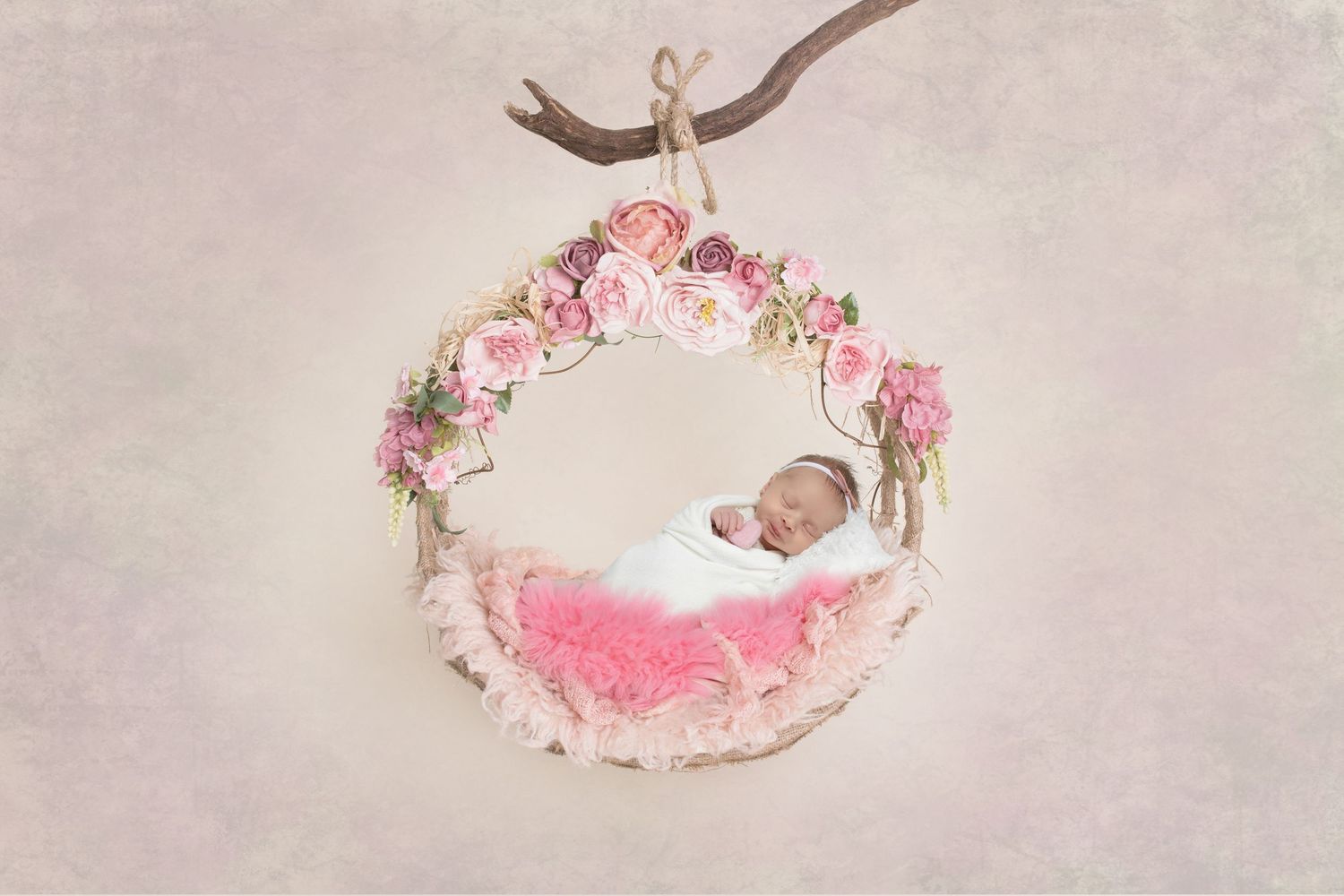 Pink floral wreath-style newborn photography prop with soft fabric nestled on branch against neutral background.