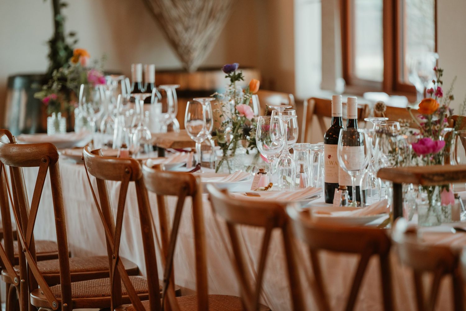 Elegant wedding reception table setting with crystal glassware and wooden cross-back chairs.