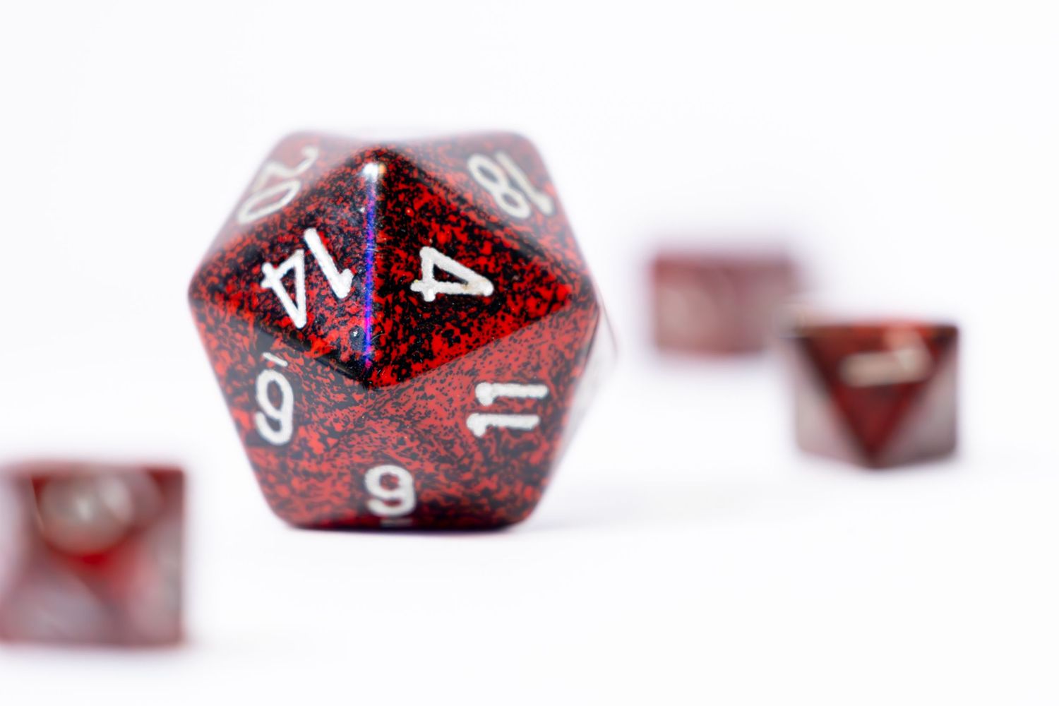 A set of red DND playing dice on a white table top with white background. The Dyson arranged where different dice are in and out of focus.