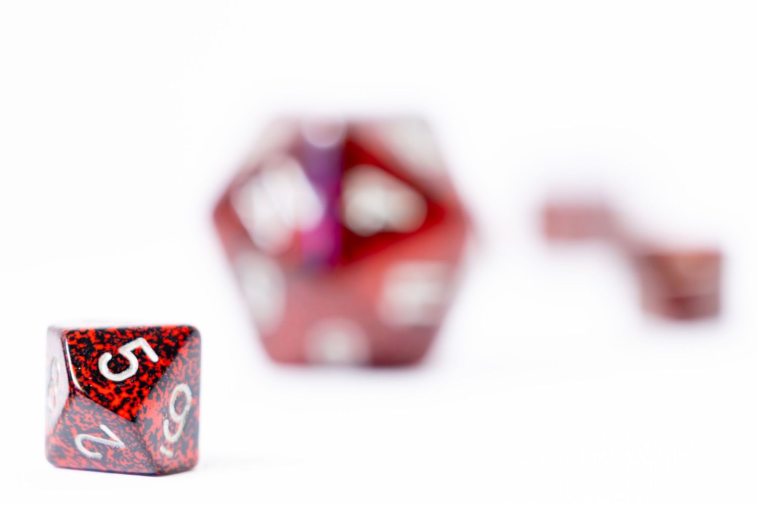 A set of red DND playing dice on a white table top with white background. The Dyson arranged where different dice are in and out of focus.