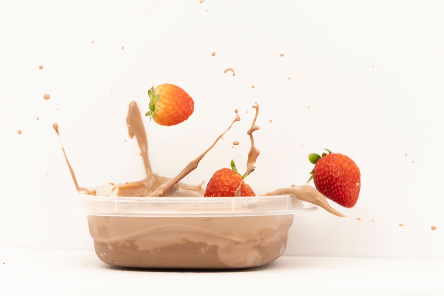 Strawberries falling into a bowl of pudding, creating a dramatic splash on a white table with white background