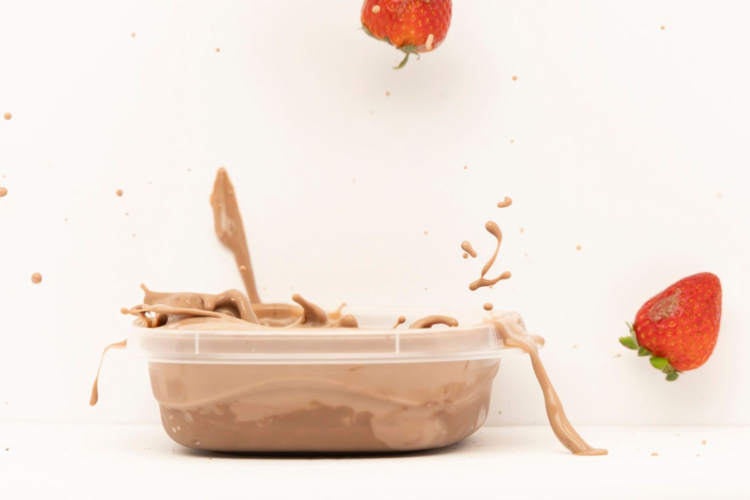 Strawberries falling into a bowl of pudding, creating a dramatic splash on a white table with white background