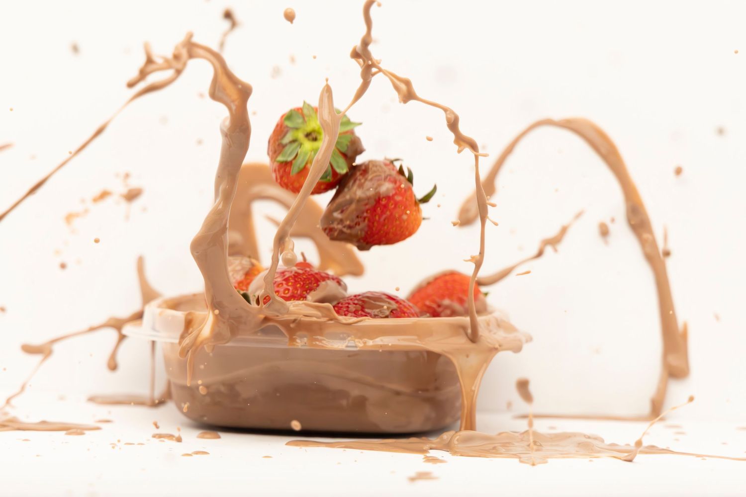 Strawberries falling into a bowl of pudding, creating a dramatic splash on a white table with white background