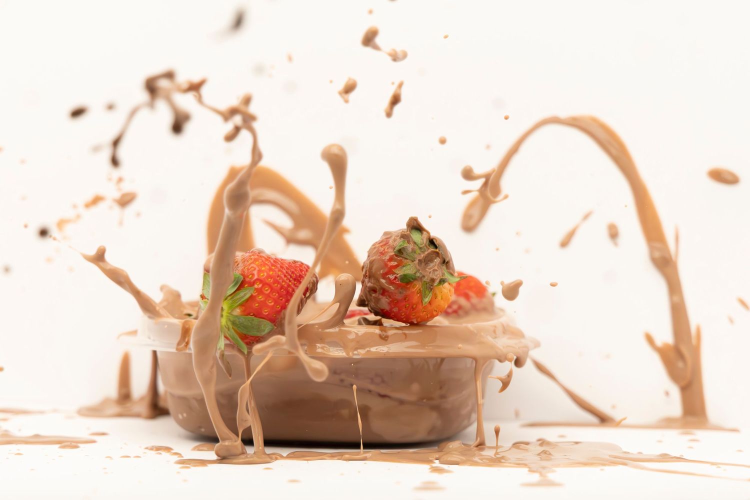 Strawberries falling into a bowl of pudding, creating a dramatic splash on a white table with white background