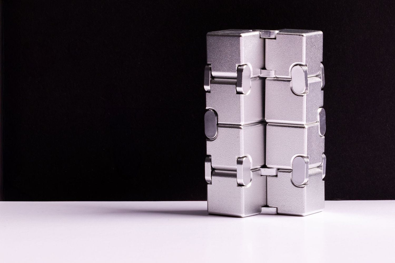 Product placement shot involving a fidget toy, which is a metal never-ending block that changes shape on a black background white table