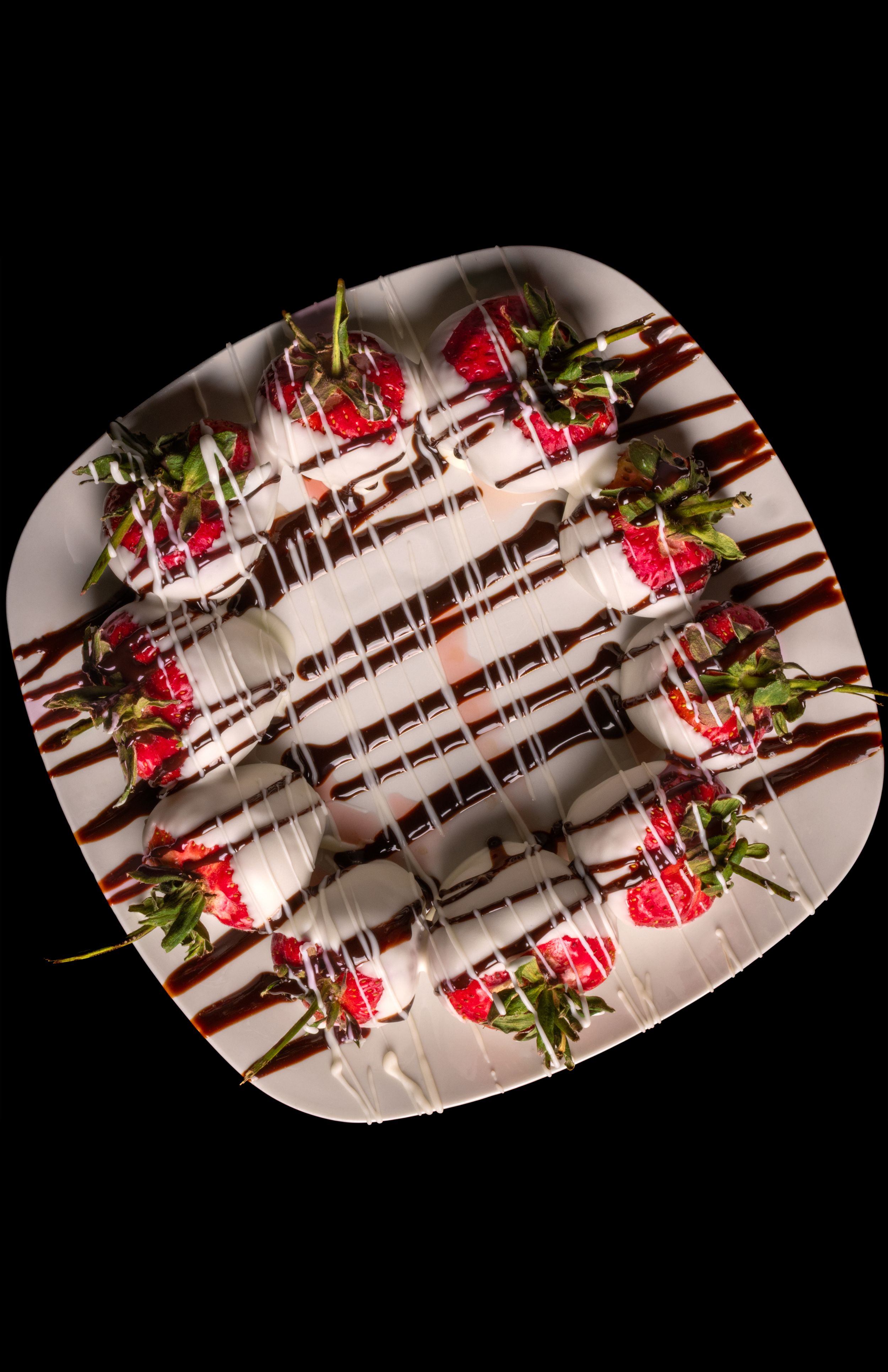 Overhead photo of strawberries drizzled with white and chocolate sauce on a white plate.