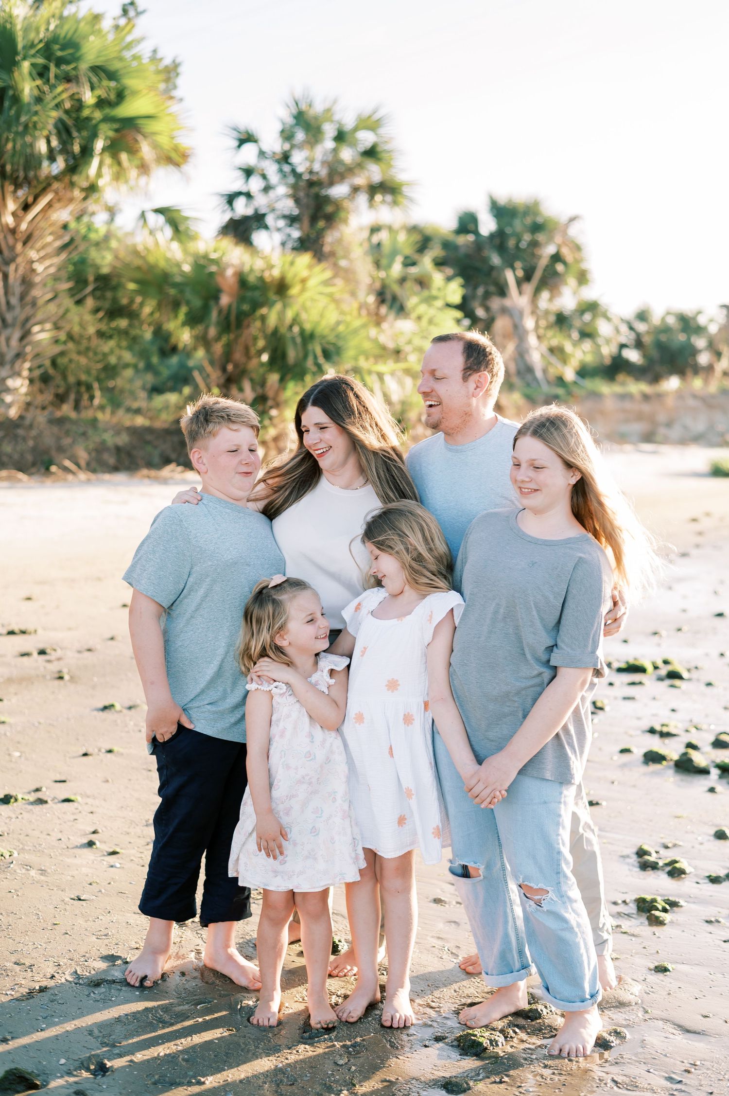 A family sharing a joyful moment together on a sunny beach with palm trees in the background.