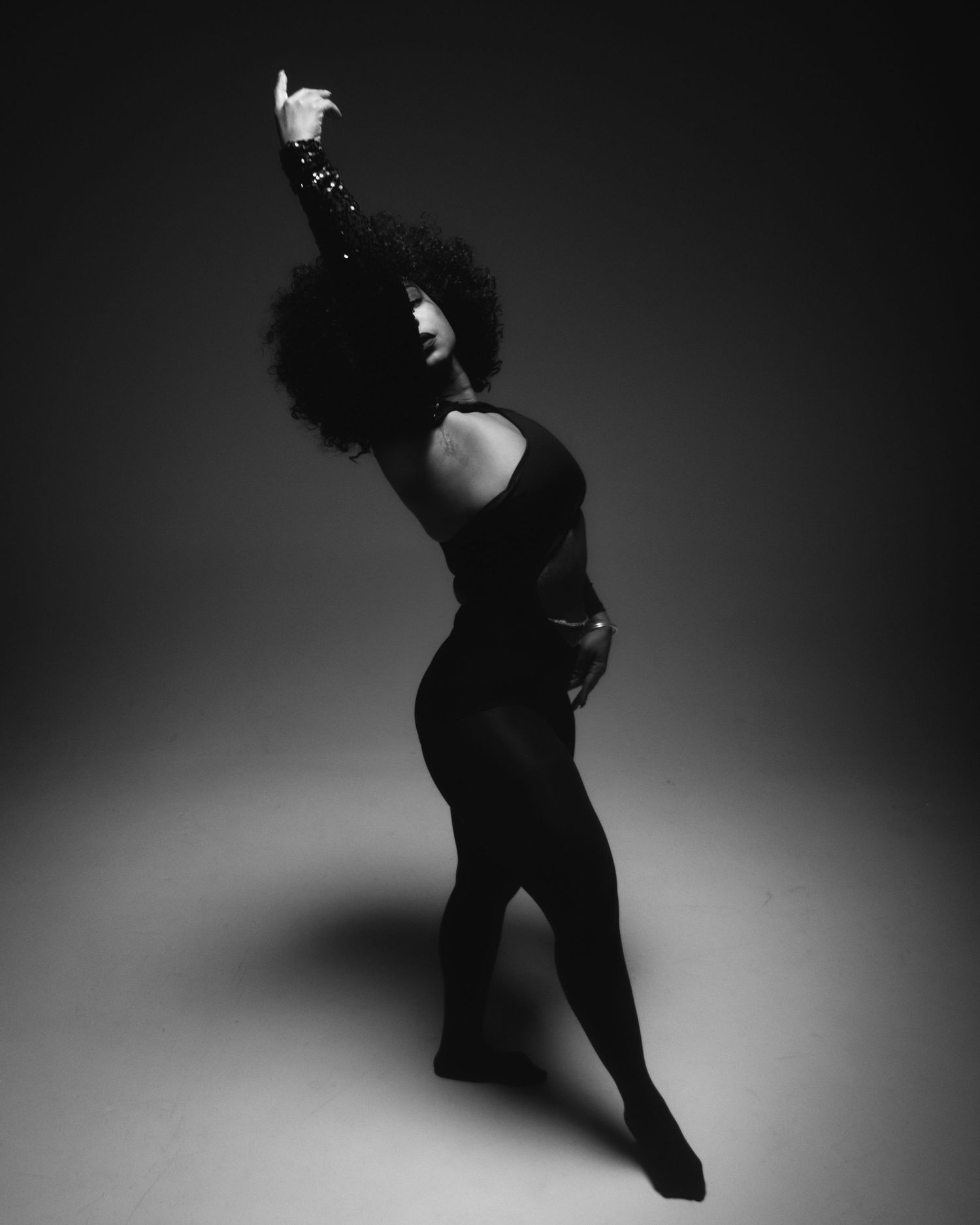 Dramatic black and white dance pose with raised arm against dark background.