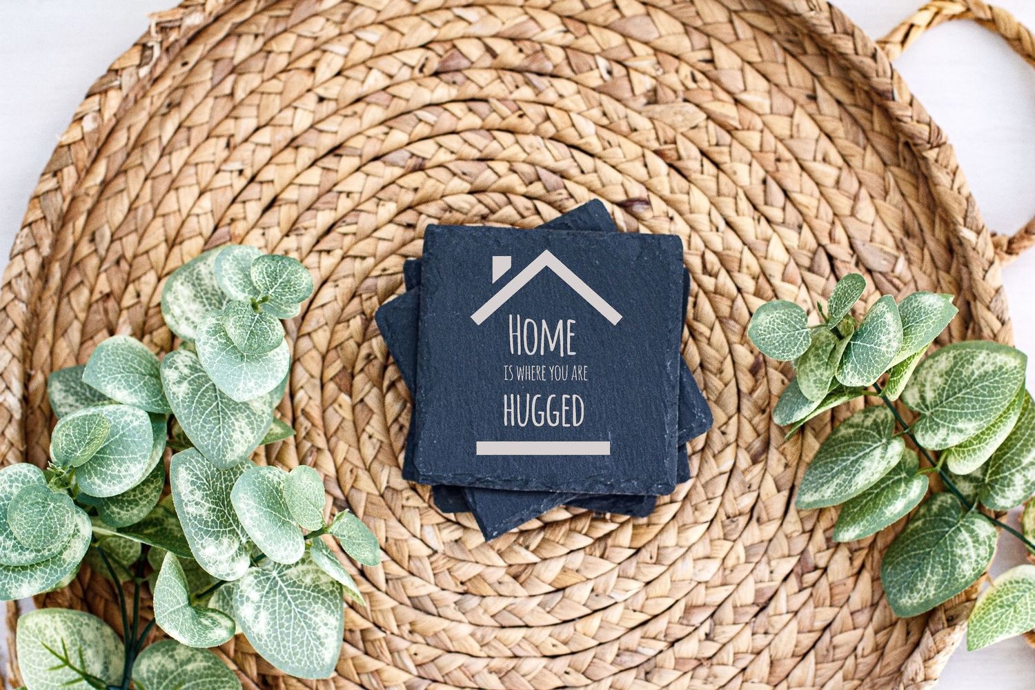 Slate coaster with house logo and text displayed on circular woven placemat with greenery.