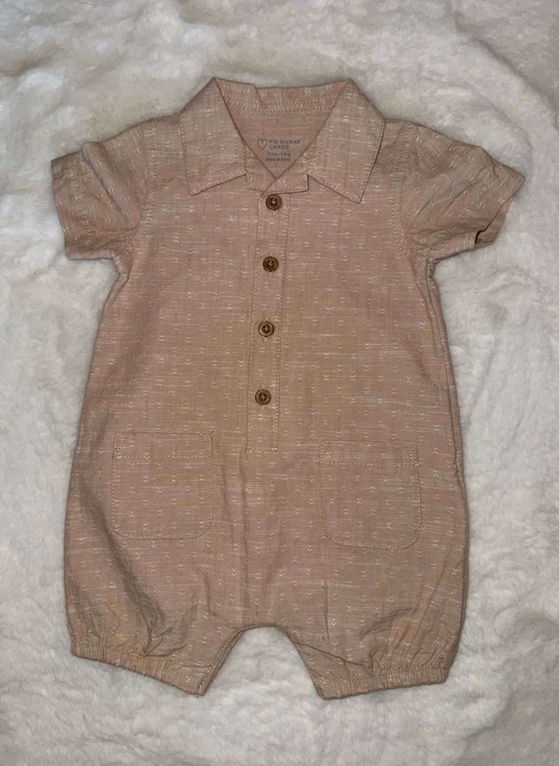 Tan linen baby romper with collar and button front closure.