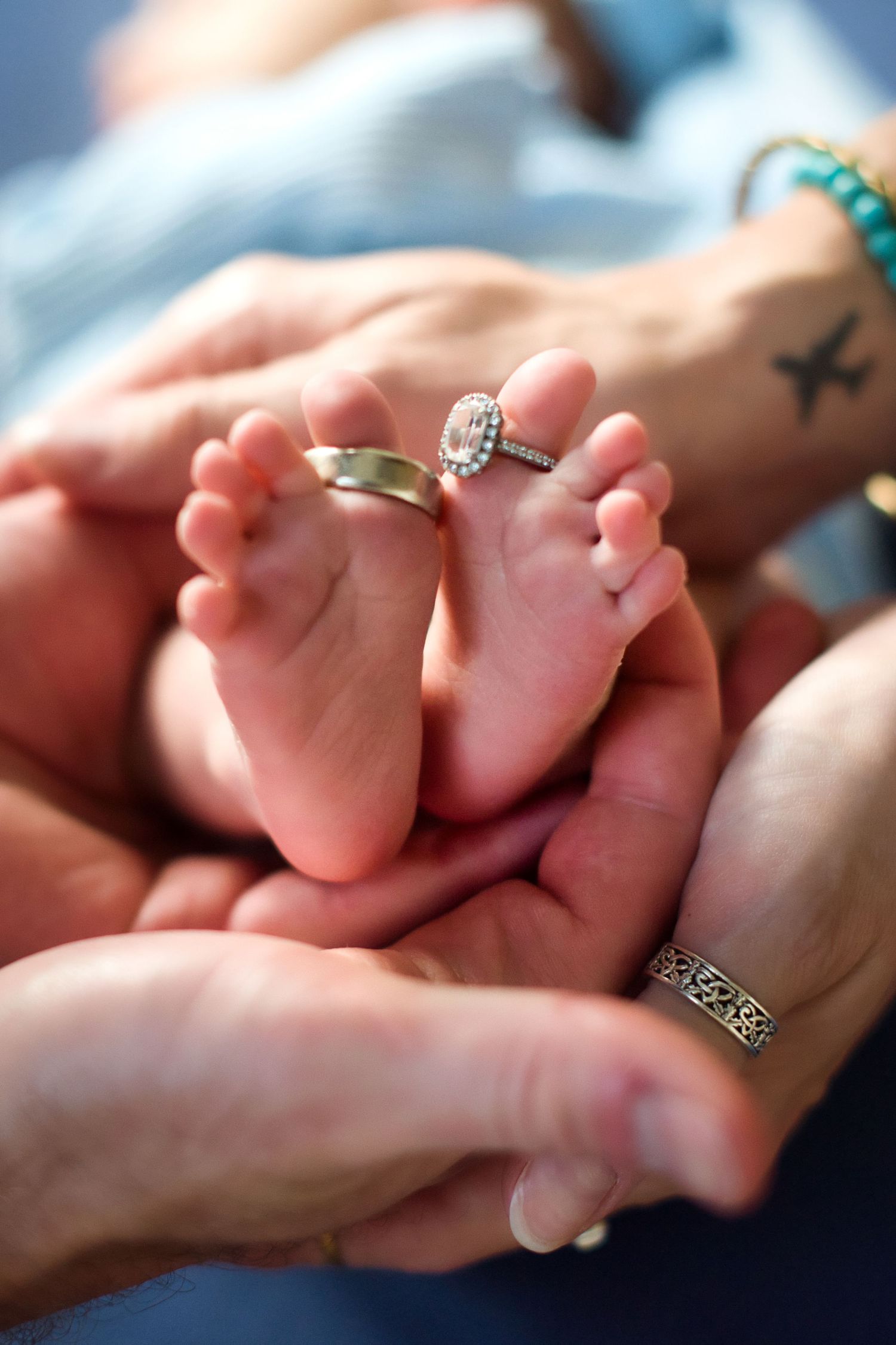 Close-up of tiny baby feet being gently held with engagement ring visible.