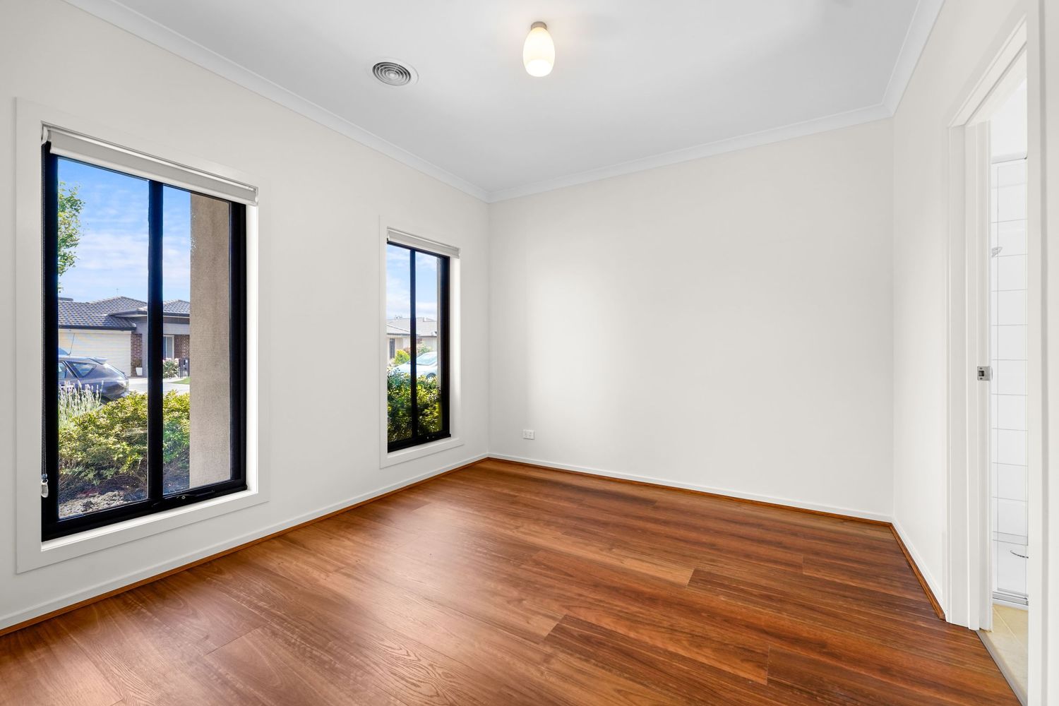Empty room with polished hardwood floors, white walls, and large windows letting in natural light.